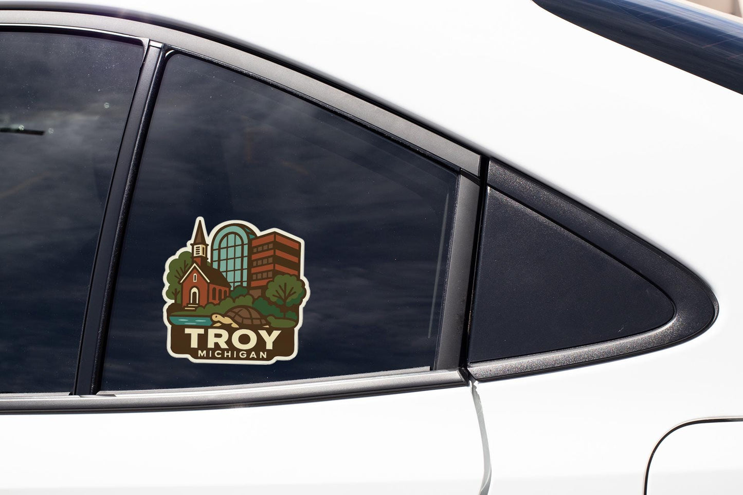 A sticker on the side of a car window, depicting a scenic view of Troy, Michigan.