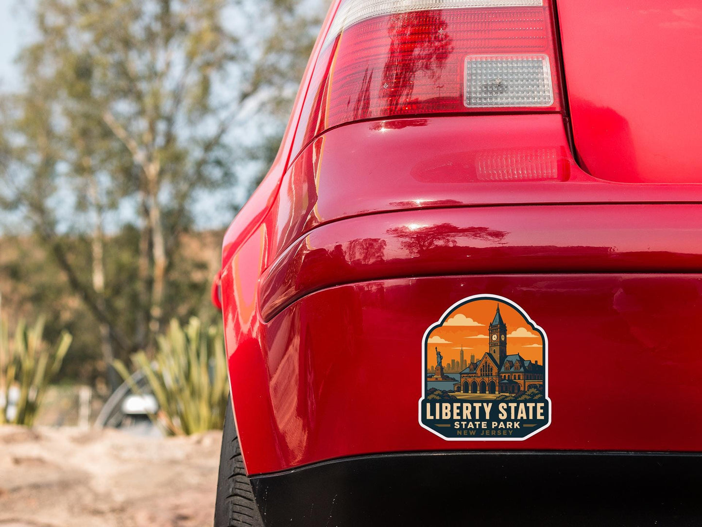the rear end of a red car with a sticker on the trunk that says "Liberty State State Park".