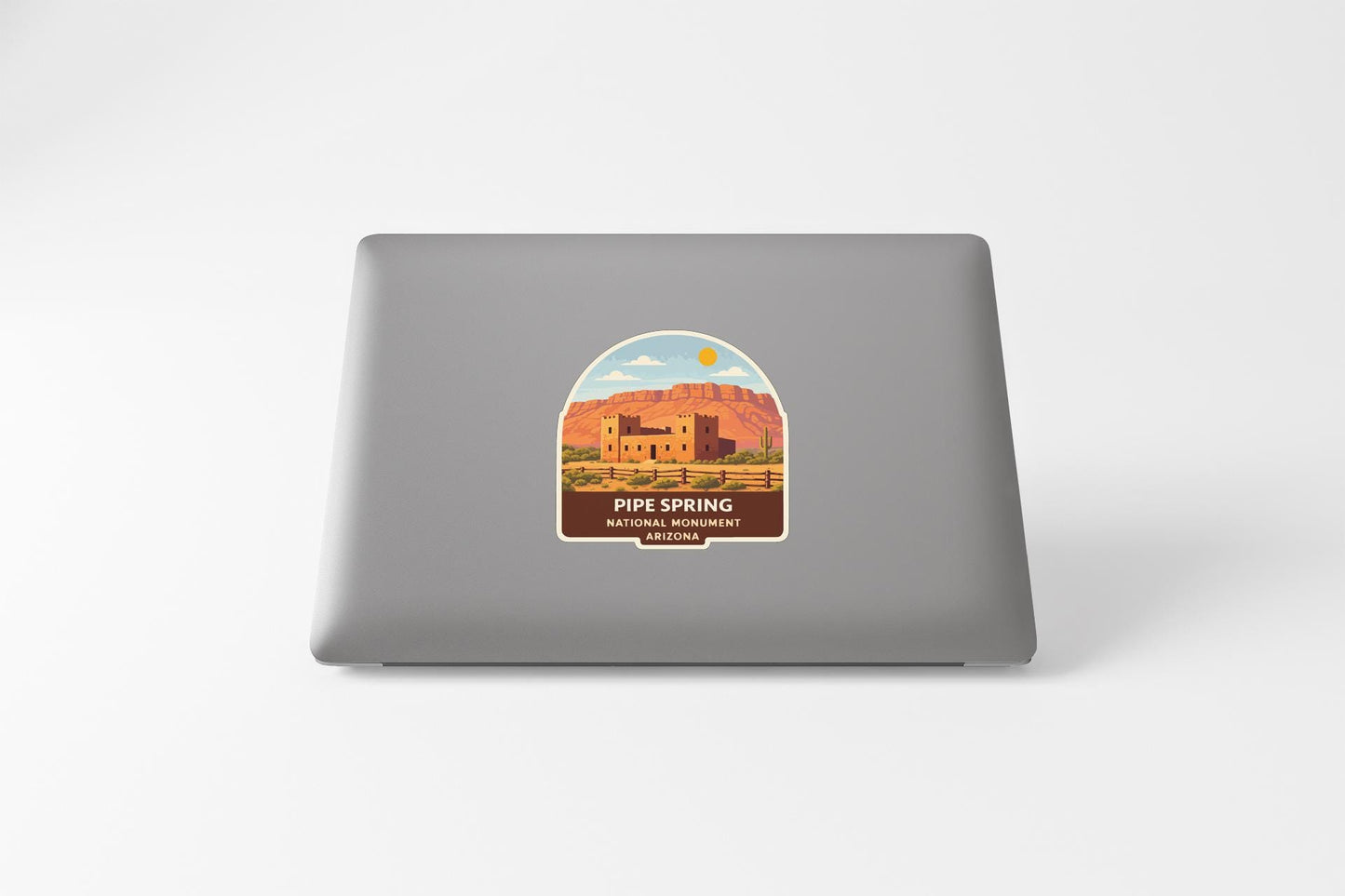 a sticker on the back of a laptop, depicting a desert landscape with a building and mountains in the background.