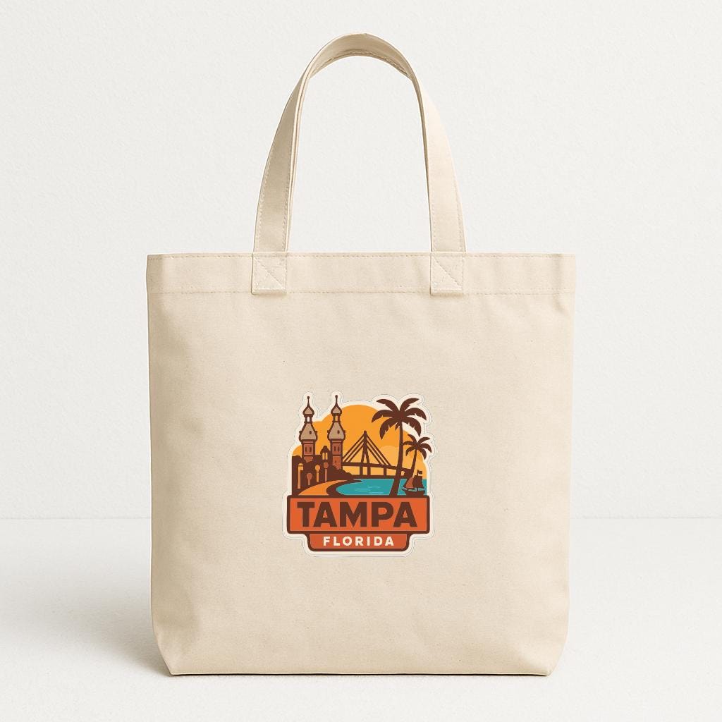 A beige tote bag with a printed design of a city skyline and palm trees, along with the text "TAMPA FLORIDA".