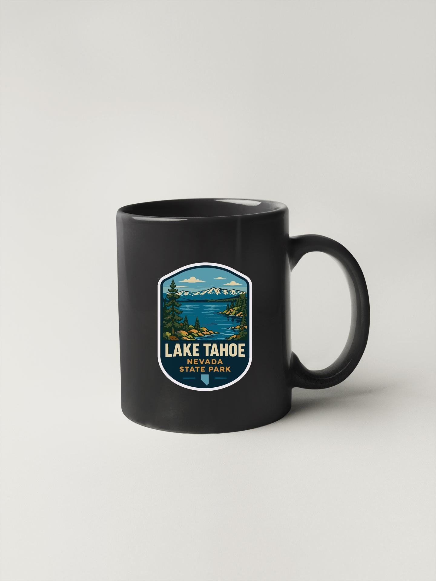 A black coffee mug with a graphic design depicting Lake Tahoe State Park.
