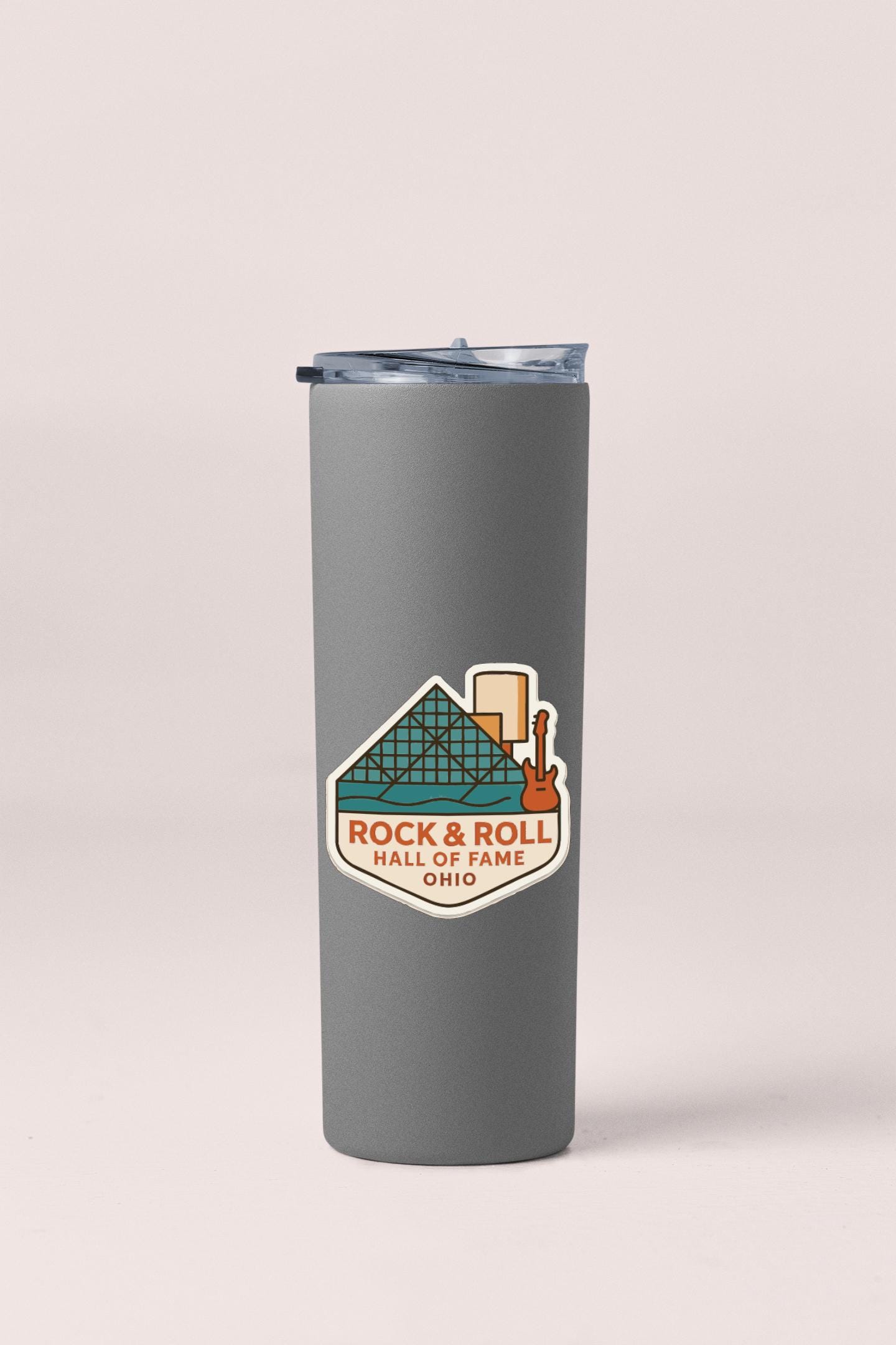A gray insulated tumbler with a sticker on it, featuring an illustration of a roller coaster and the text "Rock & Roll Hall of Fame Ohio".