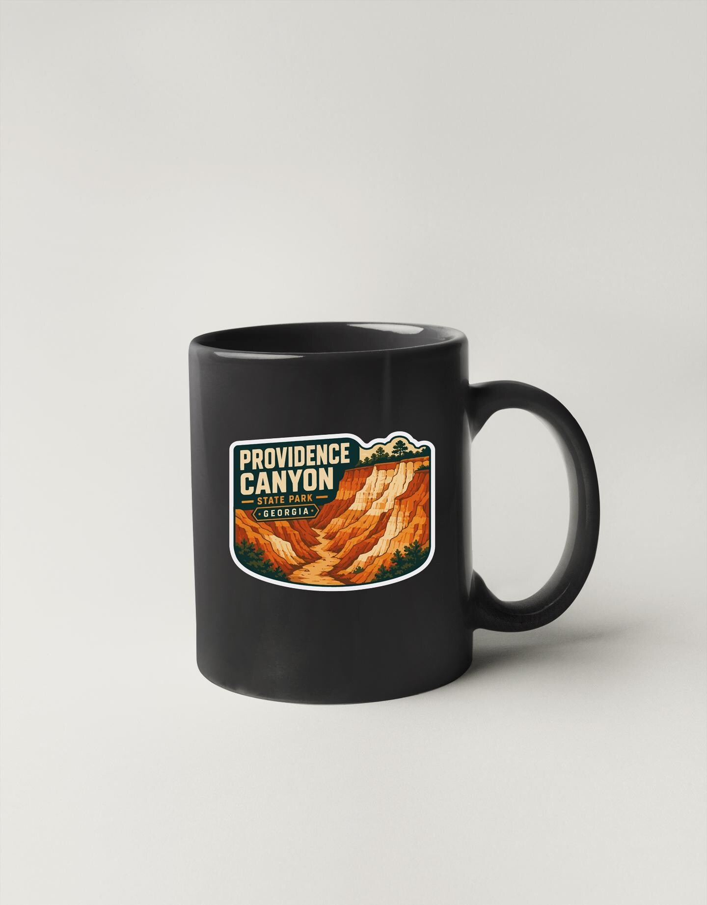 A black coffee mug with a graphic design depicting the Providence Canyon in Georgia.