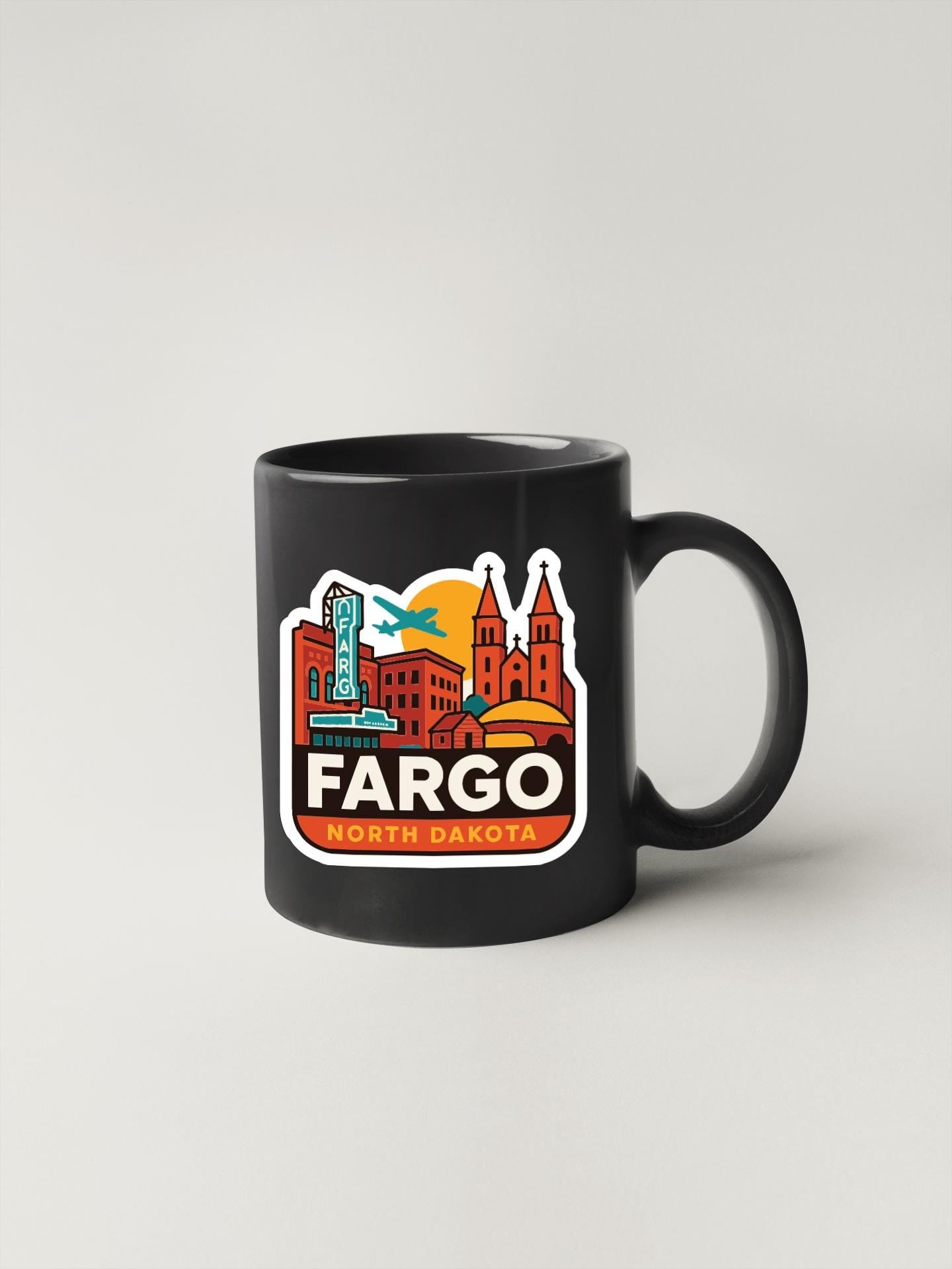 A black coffee mug with a colorful graphic depicting the downtown area of Fargo, North Dakota.