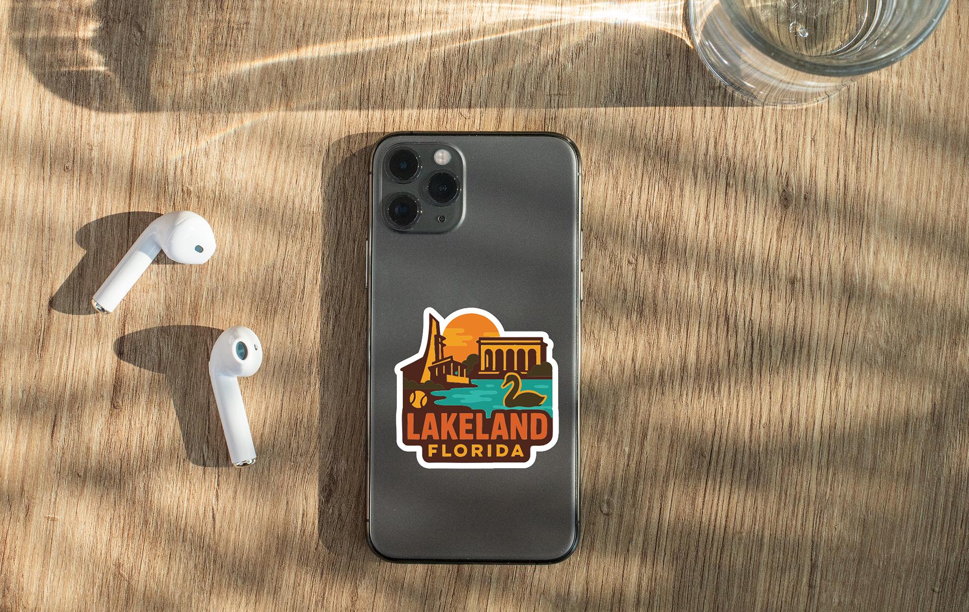 a smartphone with a sticker on the back, placed on a wooden surface alongside a pair of white earbuds and a glass of water.