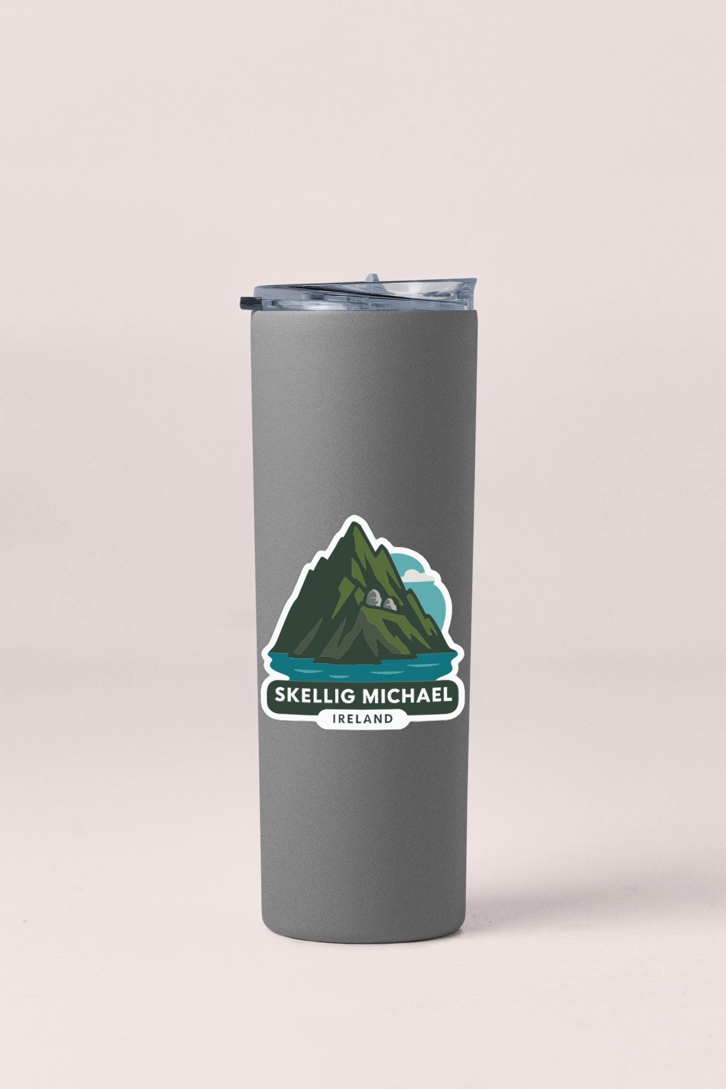 A gray tumbler with a sticker depicting a mountain and a lake, along with the text "SKELLI G MICHEL".