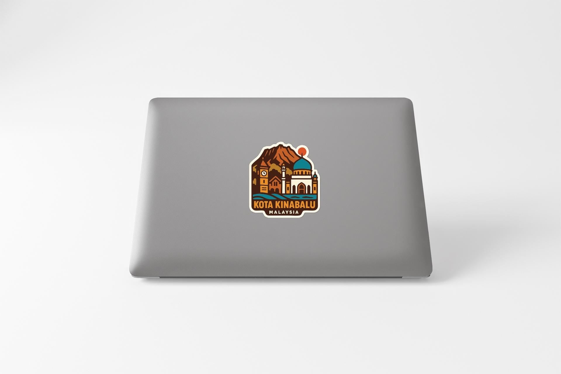 A sticker on the back of a laptop, depicting a mountain landscape with a building and a clock.