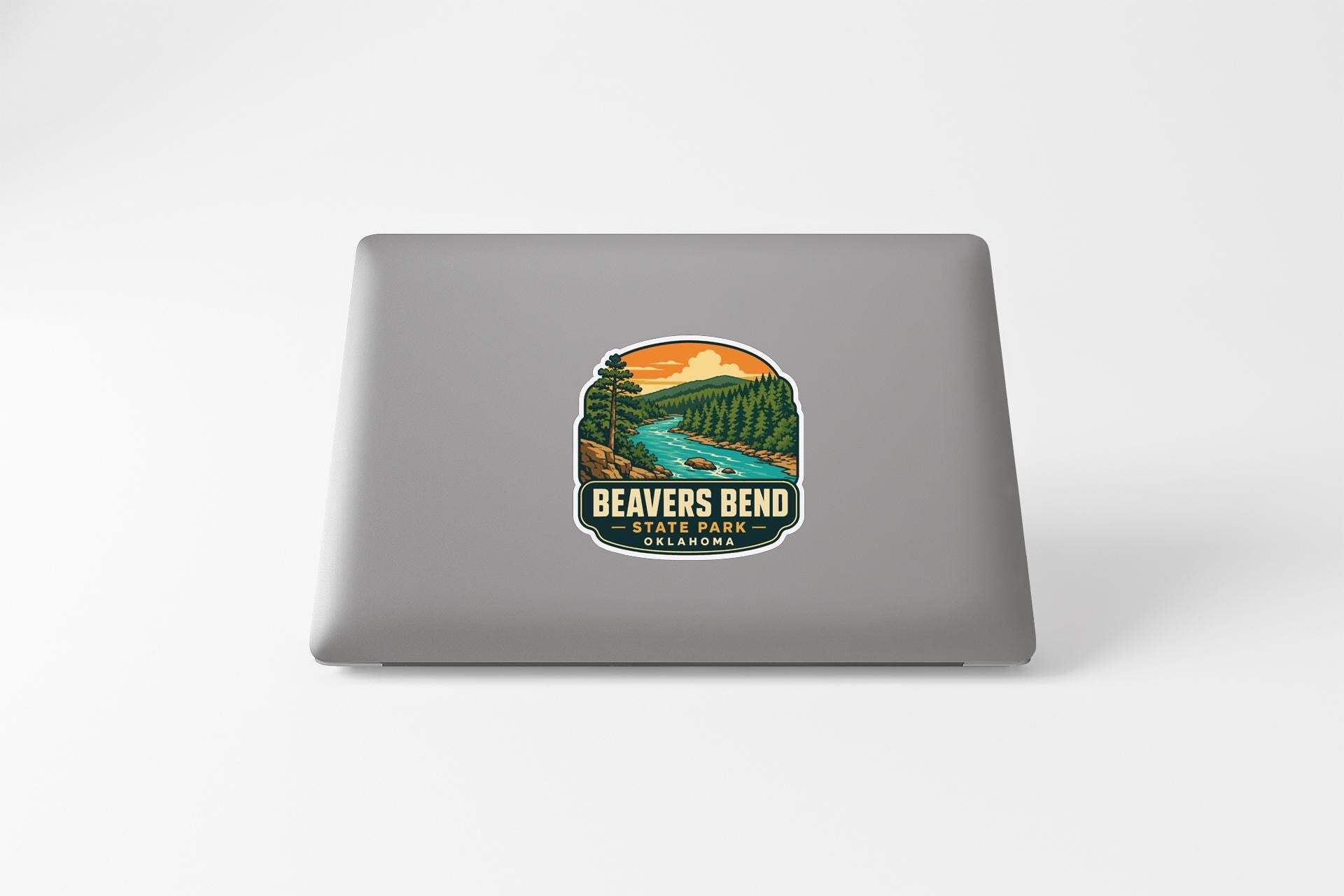 a sticker on a laptop that depicts a scenic landscape with a river, trees, and mountains.