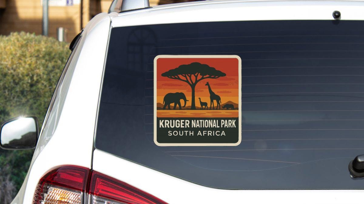 a sticker on the rear window of a car, depicting a silhouette of an elephant and a giraffe against a sunset background, with the text "KRUGER NATIONAL PARK SOUTH AFRICA".