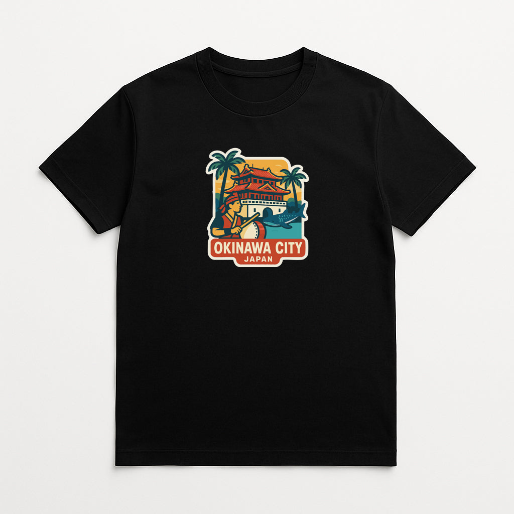 A black t-shirt with a colorful graphic design depicting a temple, palm trees, and a sunset. The text "OKINAWA CITY JAPAN" is displayed below the graphic.