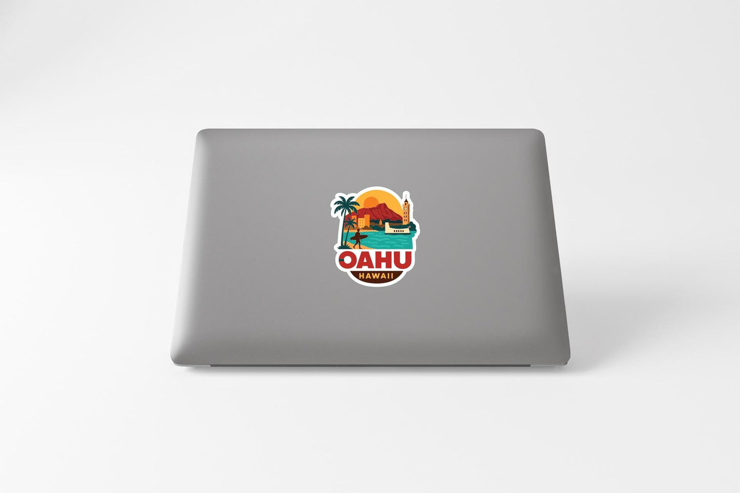 A sticker on the back of a laptop displaying a tropical beach scene with palm trees, a sunset, and a mountain.
