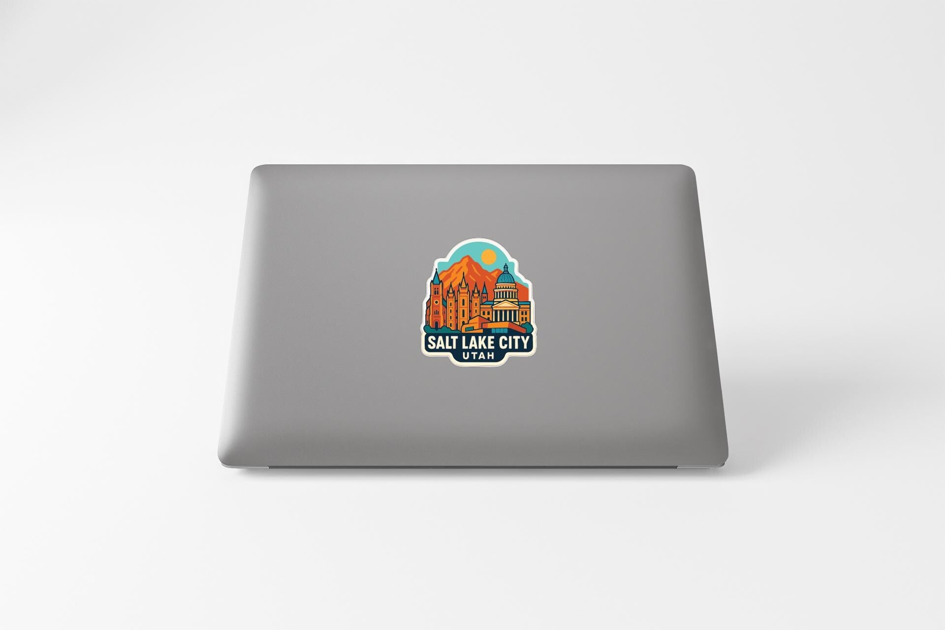 A sticker depicting a cityscape with a mountain in the background, placed on the back of a laptop.