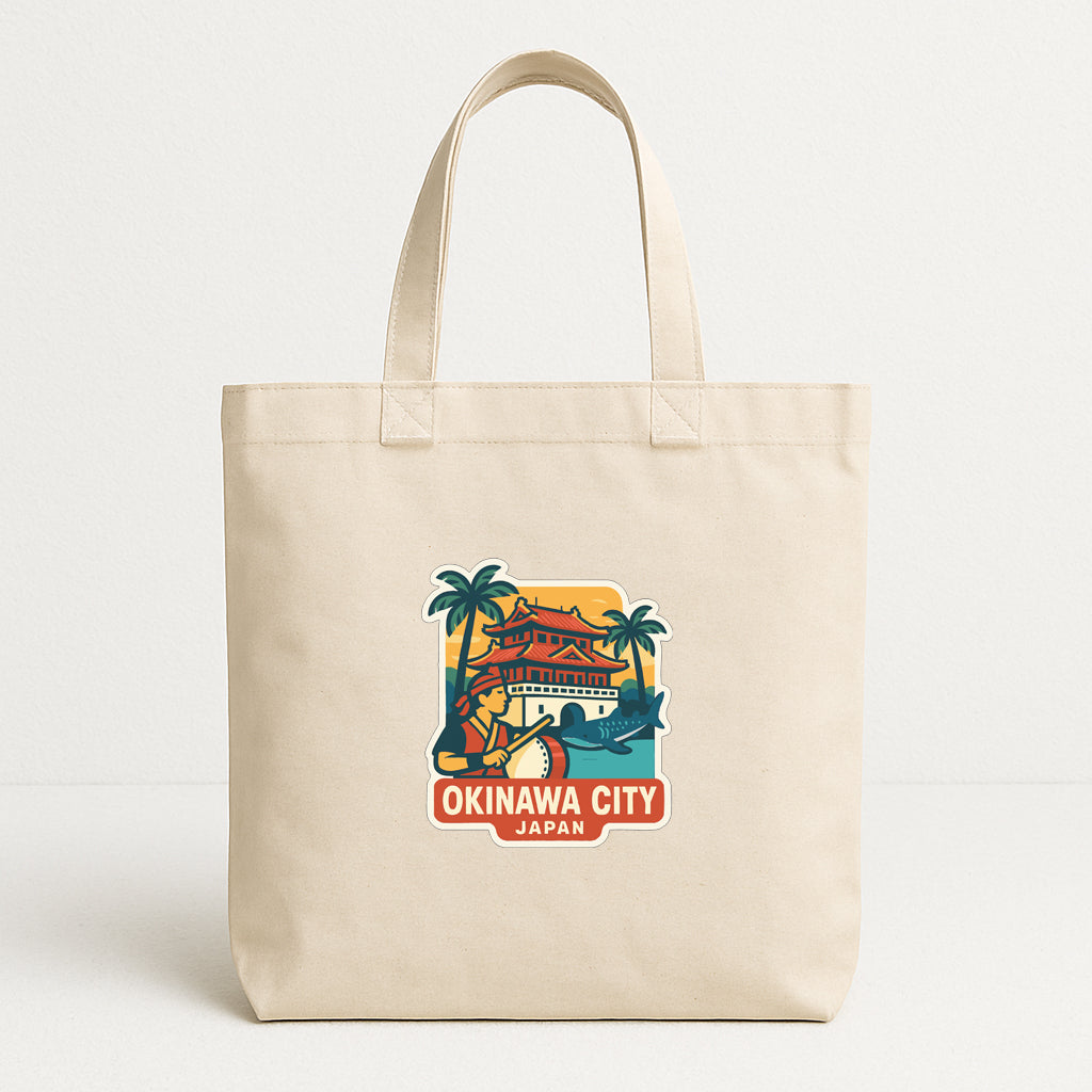 A beige tote bag with a printed design depicting a tropical scene and the text "OKINAWA CITY JAPAN" printed on it.