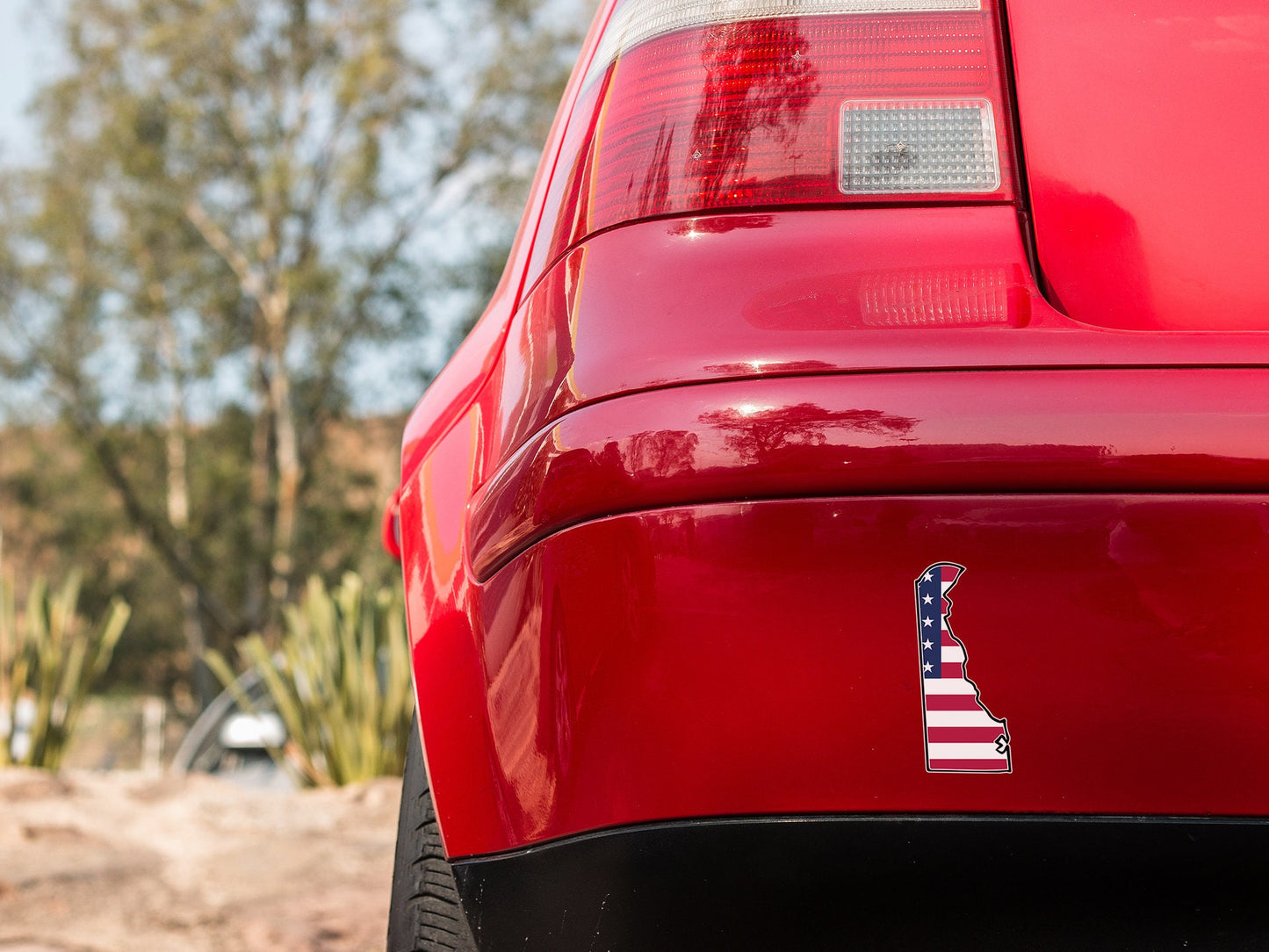 the tail end of a red car with an american flag sticker on it