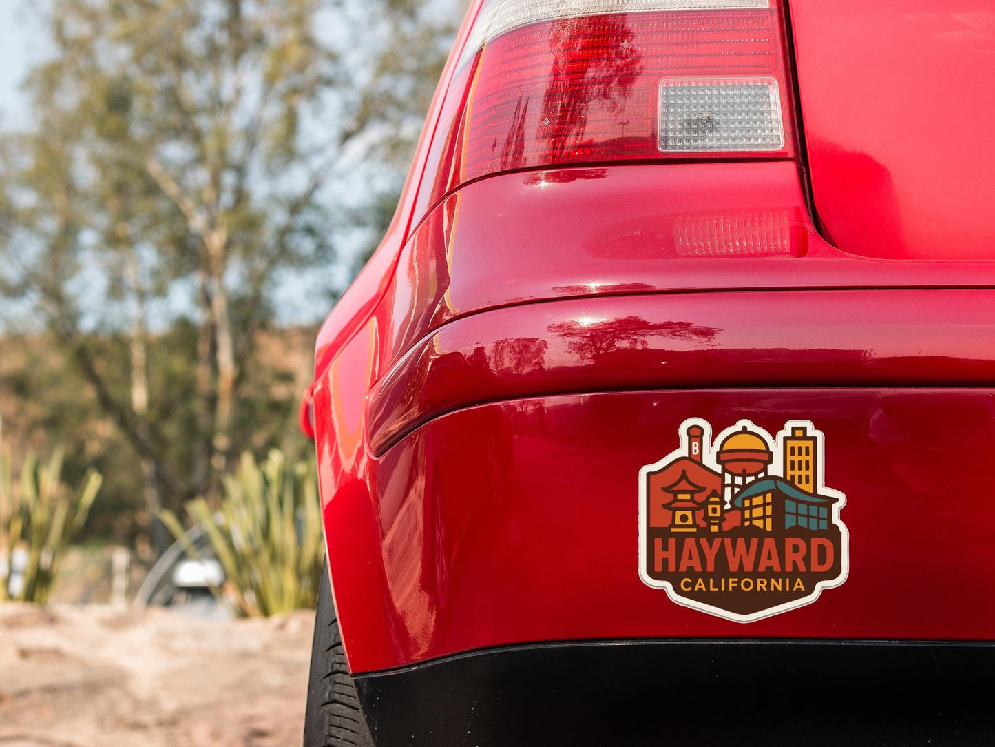 the rear end of a red car with a sticker on the trunk that says "Hayward, California".