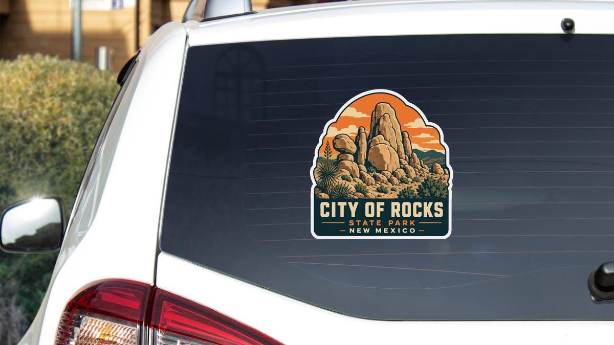 A sticker on the rear window of a white car, depicting a scenic landscape with mountains and a desert.