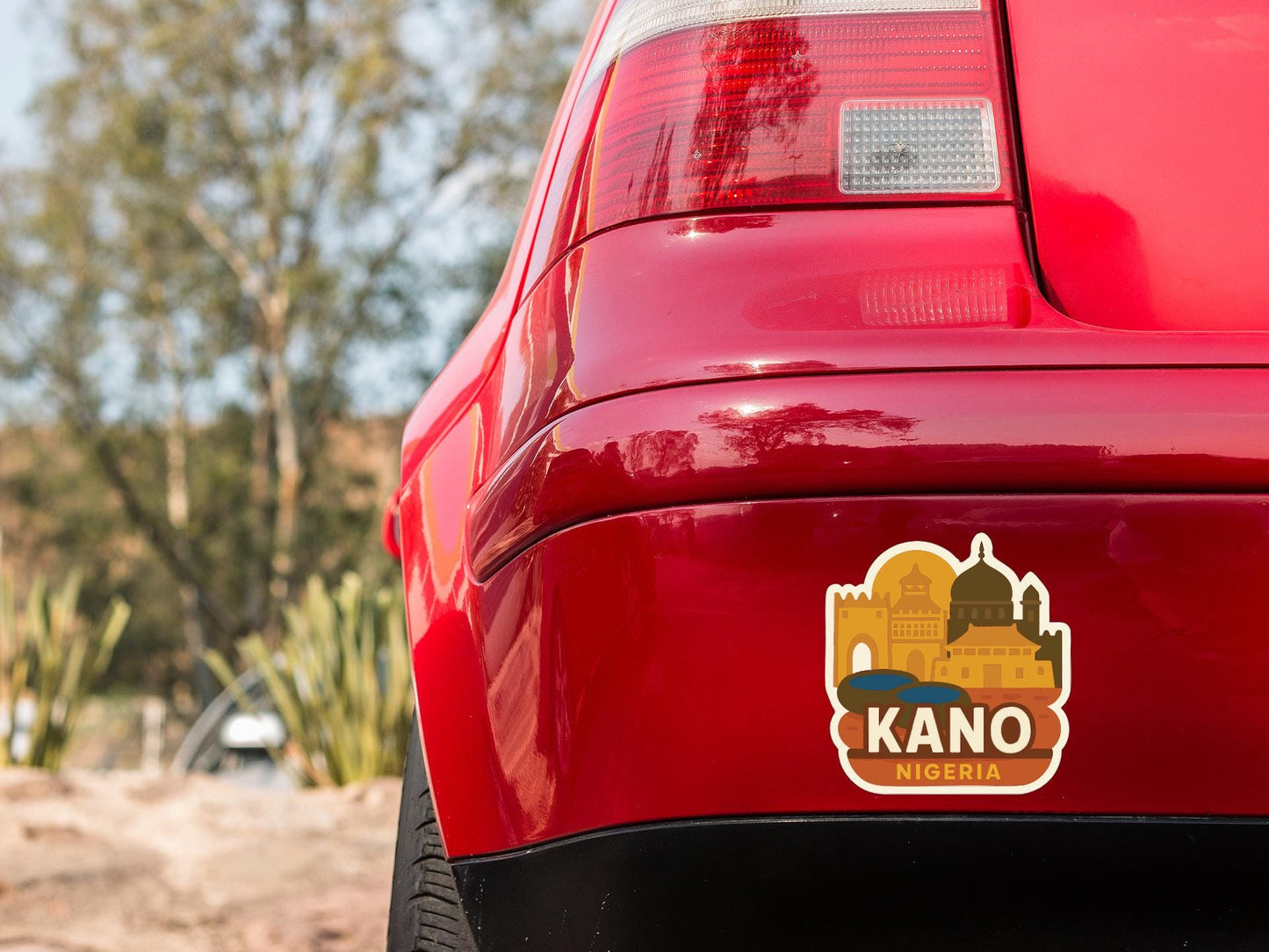 the rear end of a red car with a sticker on the back window that says "Kano Nigeria".
