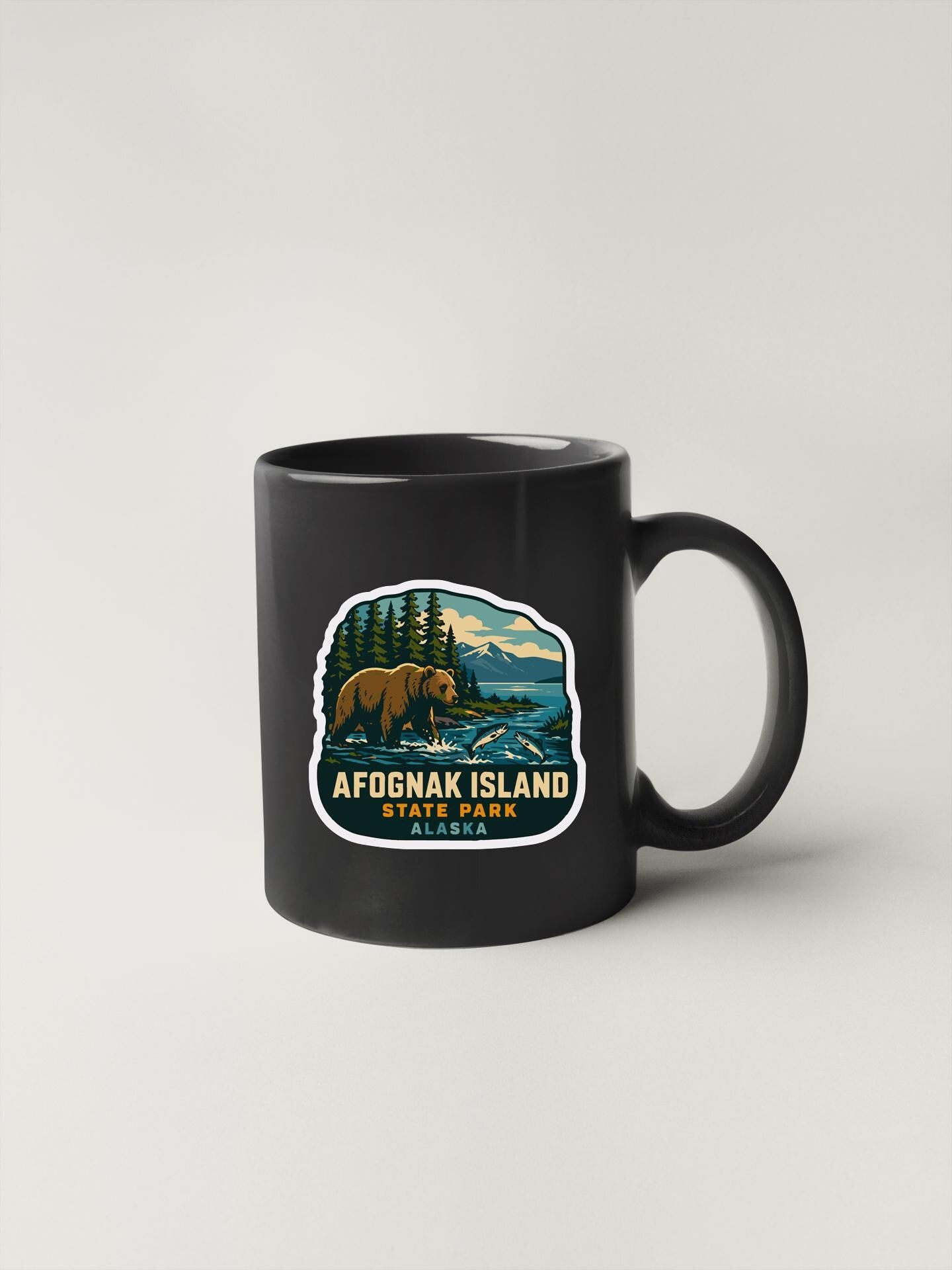A black coffee mug with a sticker depicting a bear and a scenic landscape, along with the text "AFOGNAK ISLAND STATE PARK".
