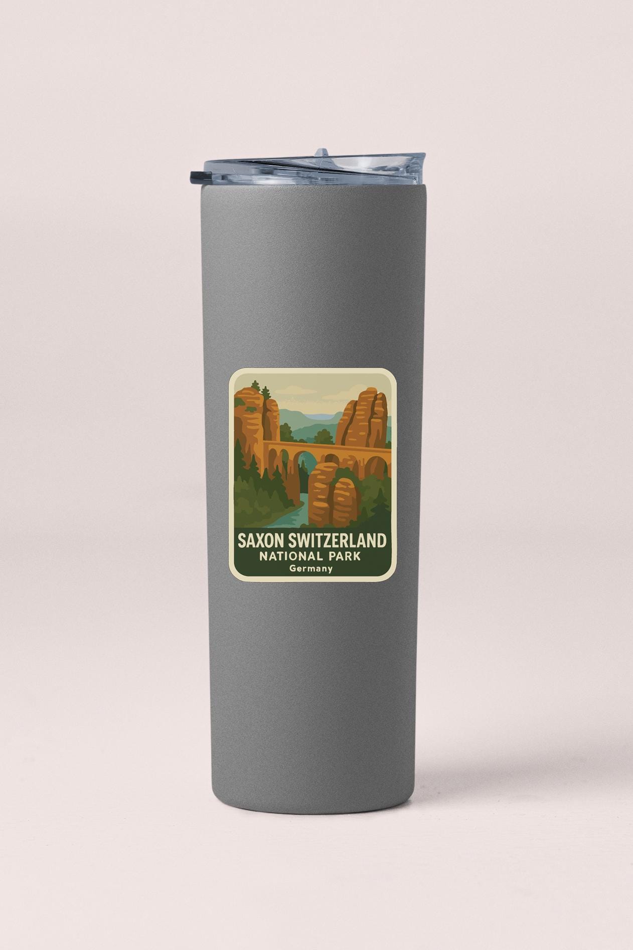 A gray tumbler with a label that features an illustration of Saxon Switzerland National Park in Germany.