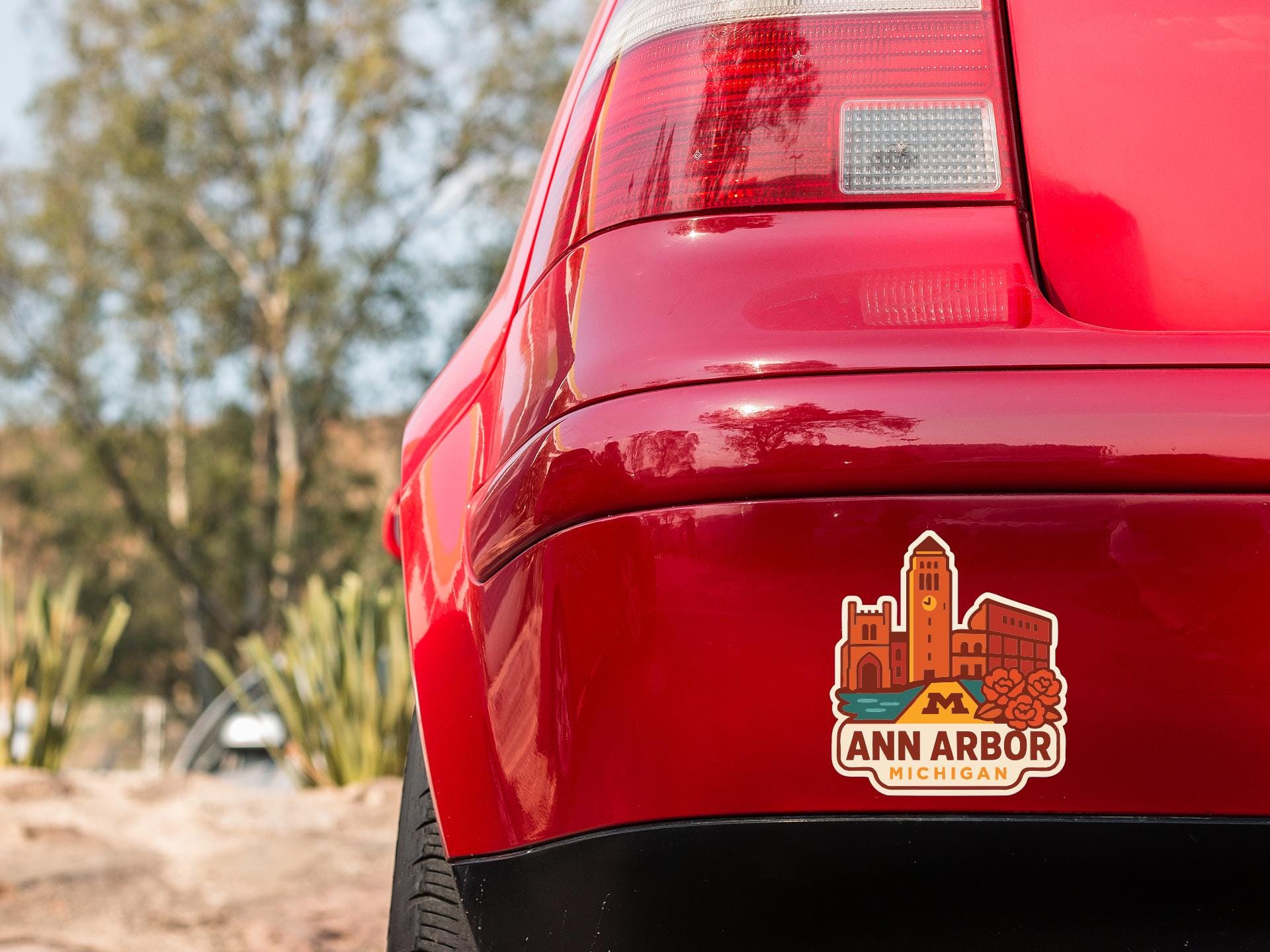 the rear end of a red car with a sticker on the trunk that features an illustration of a cityscape.