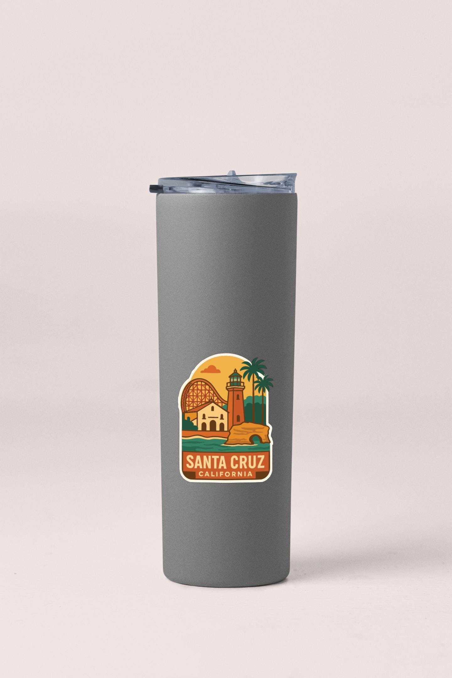A gray insulated tumbler with a sticker depicting a scenic view of Santa Cruz, California.