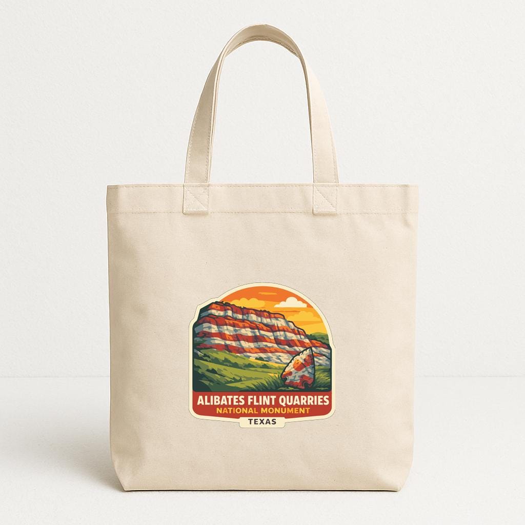 A beige tote bag with a printed design depicting a mountain landscape and the text "Alibates Flint Quarries National Monument, Texas" printed on it.