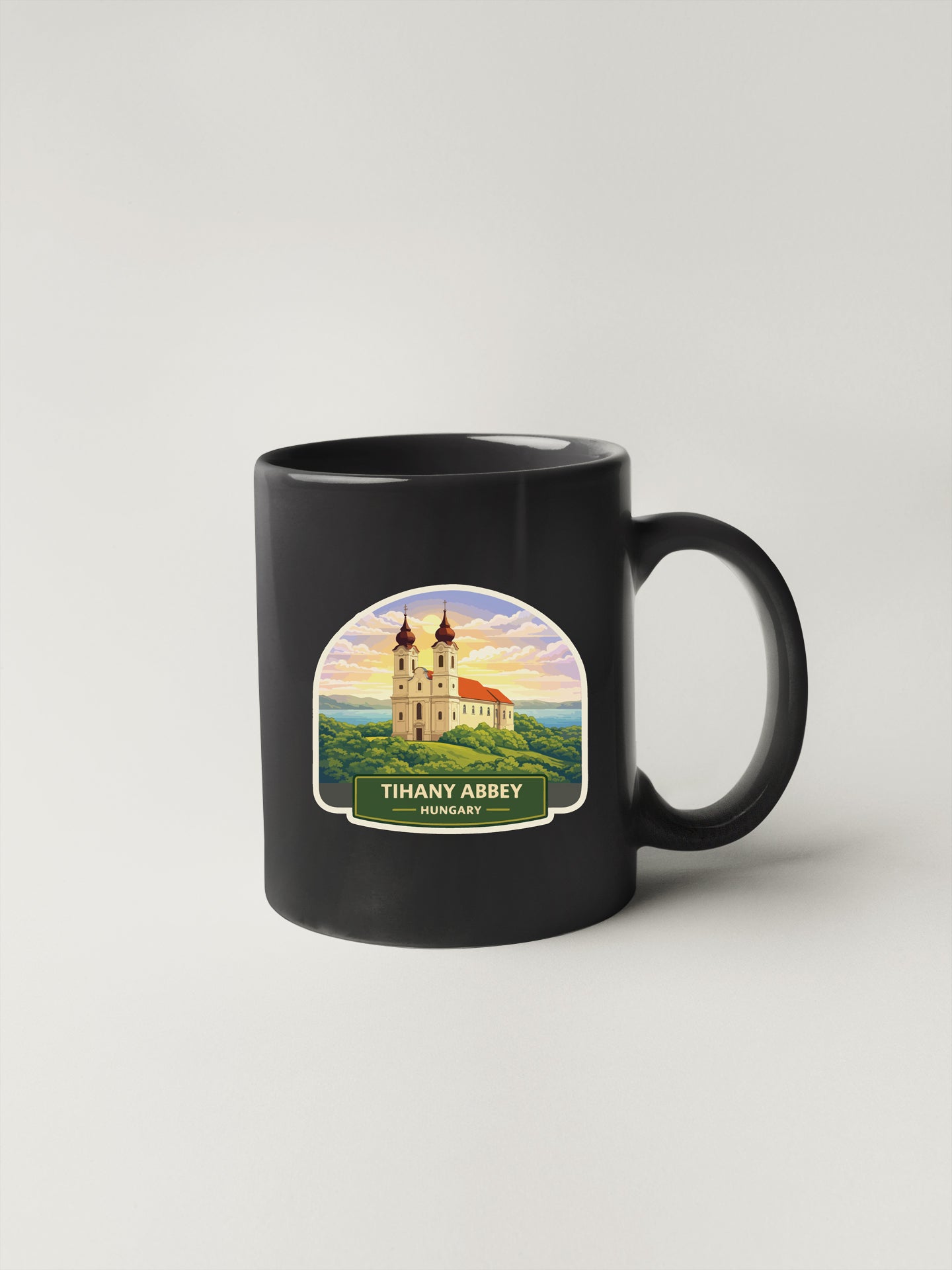 A black coffee mug with a label depicting the Tihany Abbey, a historic landmark in Hungary.