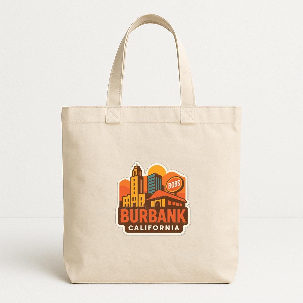 A beige tote bag with a printed design of a city skyline and the text "BURBANK CALIFORNIA" printed on it.