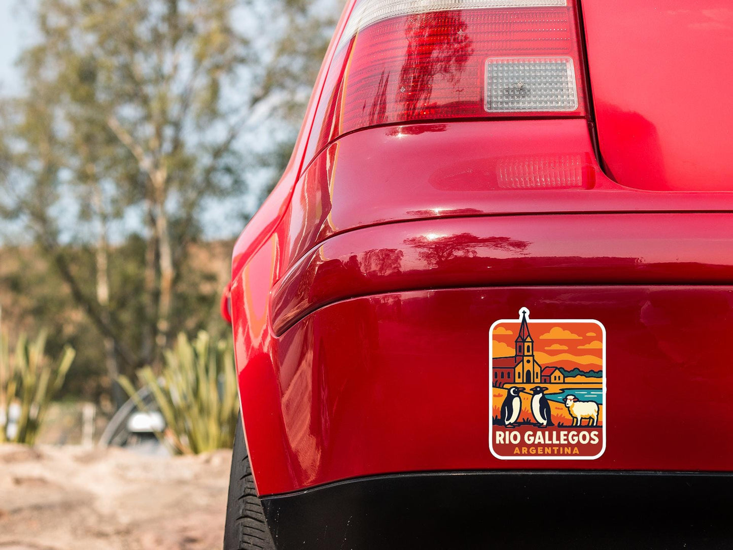 the rear end of a red car with a sticker on the back window that features a scenic image of Rio de Janeiro, Argentina.