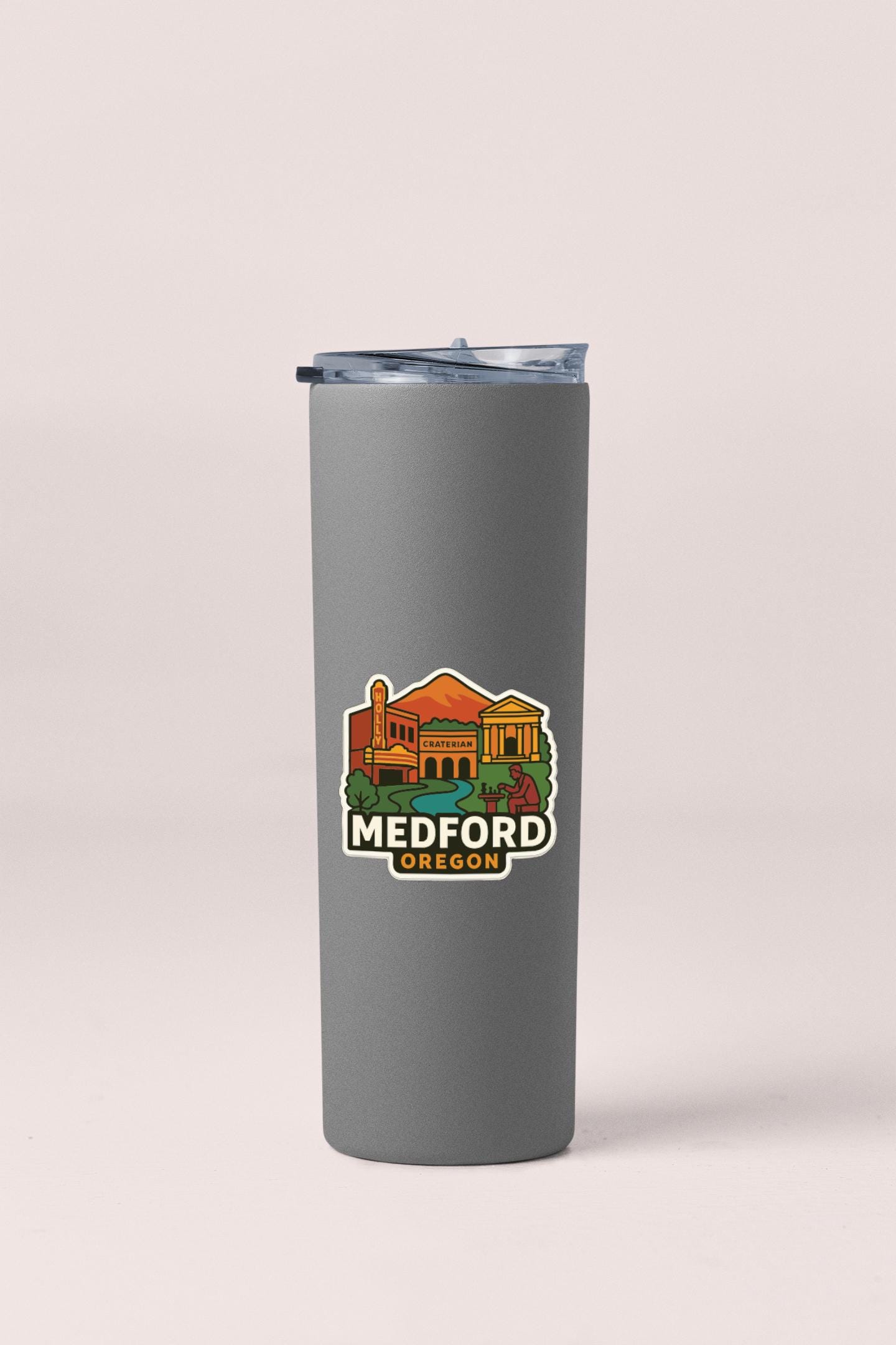 A gray insulated tumbler with a lid and a sticker featuring an illustration of a building and the text "MEDFORD OREGON".