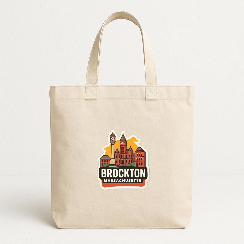 A beige tote bag with a graphic of a city skyline and the text "BROCKTON MASSACHUSETTS" printed on it.