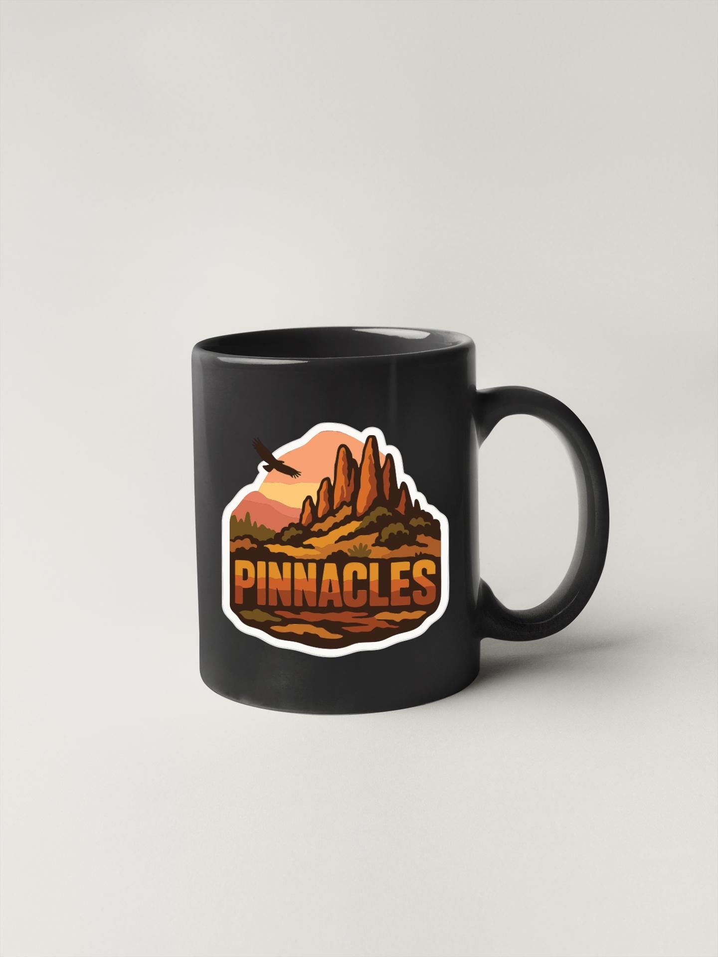 A black coffee mug with a graphic design depicting a mountain landscape with the word "PINNACLES" written on it.