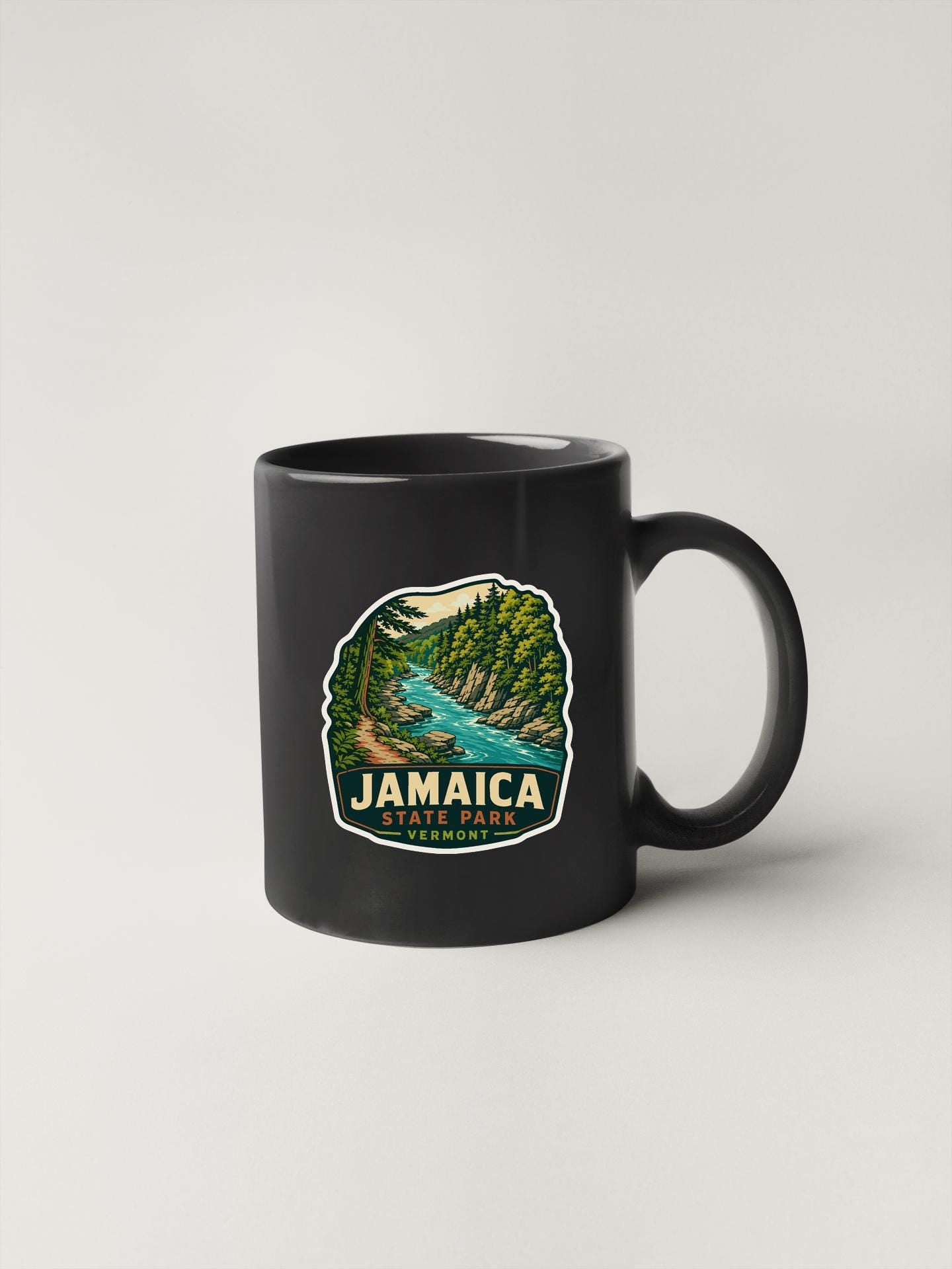 A black coffee mug with a graphic design depicting a scenic landscape with a river and trees, along with the text "JAMAICA STATE PARK VERNON".