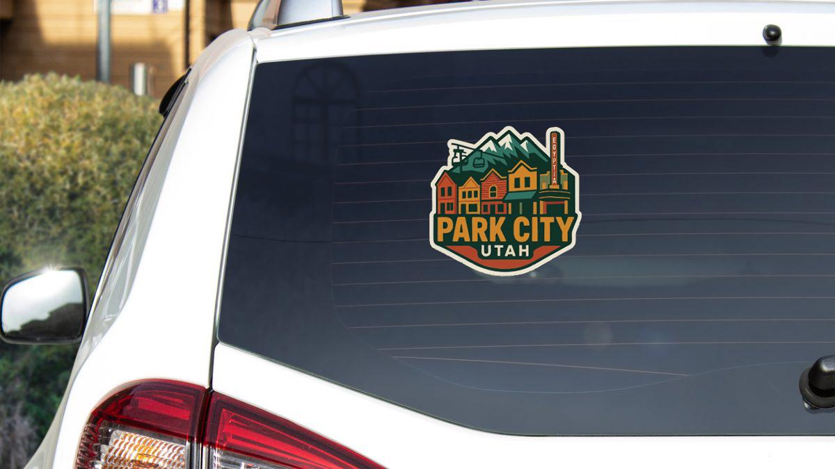 A sticker on the rear window of a white car, featuring a colorful illustration of a cityscape with mountains in the background.