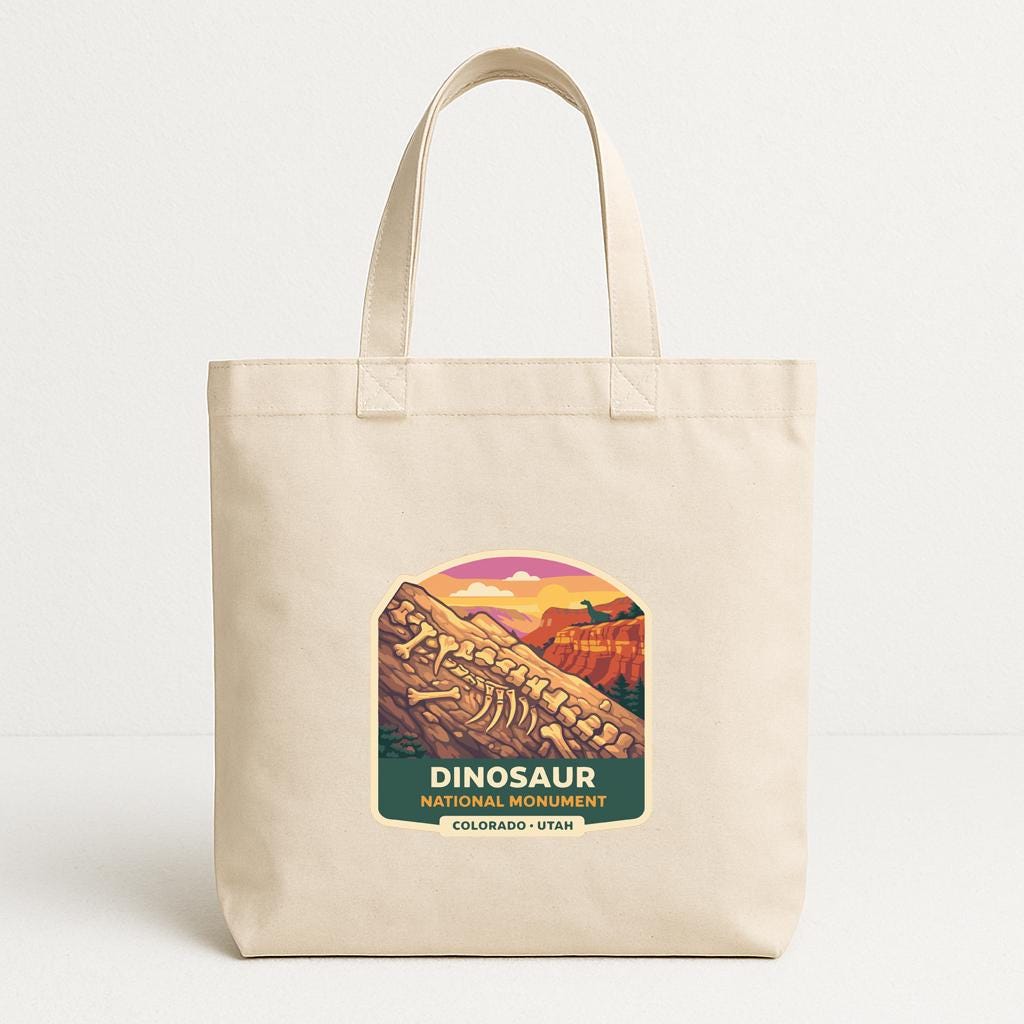 A beige tote bag with a graphic design featuring a dinosaur skeleton and the text "DINOSAUR NATIONAL PARK COLORADO - UTA".