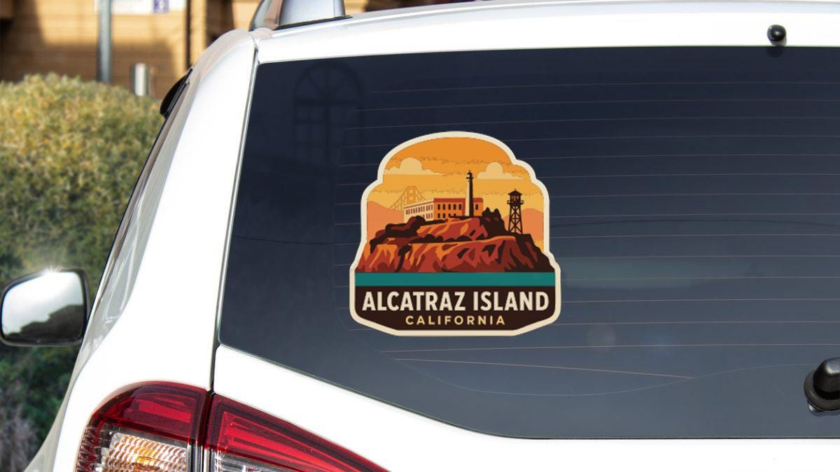A sticker on the rear window of a white vehicle, depicting a scenic landscape with a mountain and a lighthouse, representing Alcatraz Island in California.