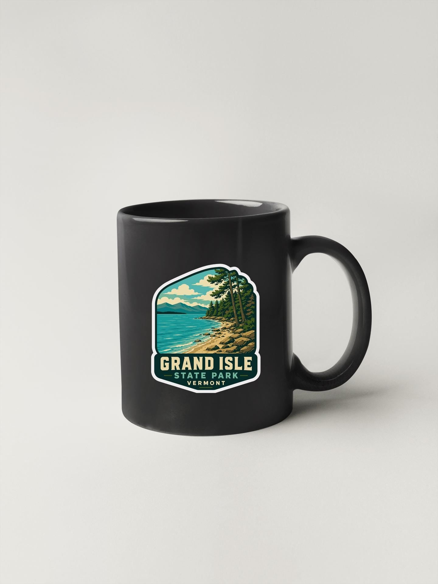 A black coffee mug with a graphic design depicting a scenic landscape featuring a lake, mountains, and trees.