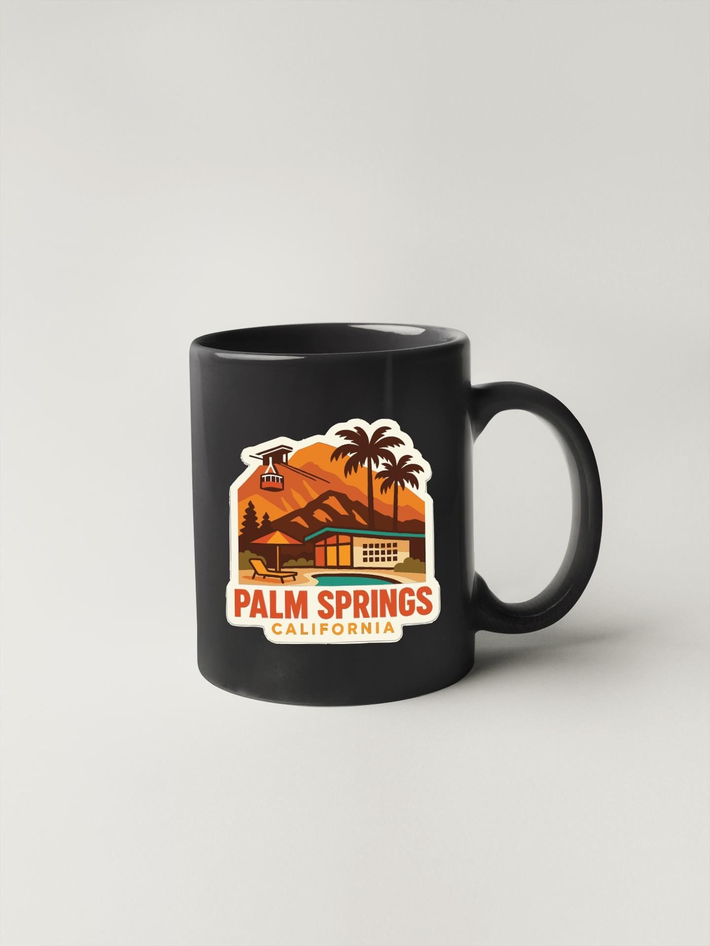 A black coffee mug with a sticker depicting a scenic view of Palm Springs, California.