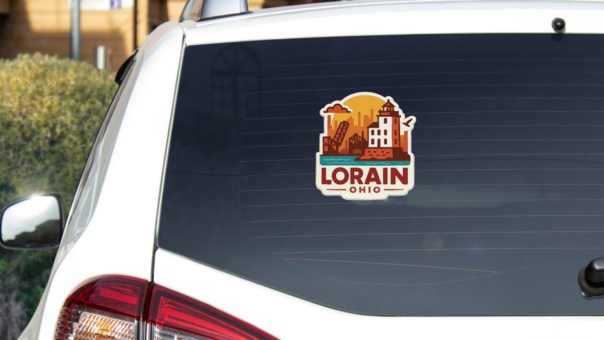 A sticker on the rear window of a white car, featuring an illustration of a cityscape with a lighthouse and the text "LORAIN, OHIO".
