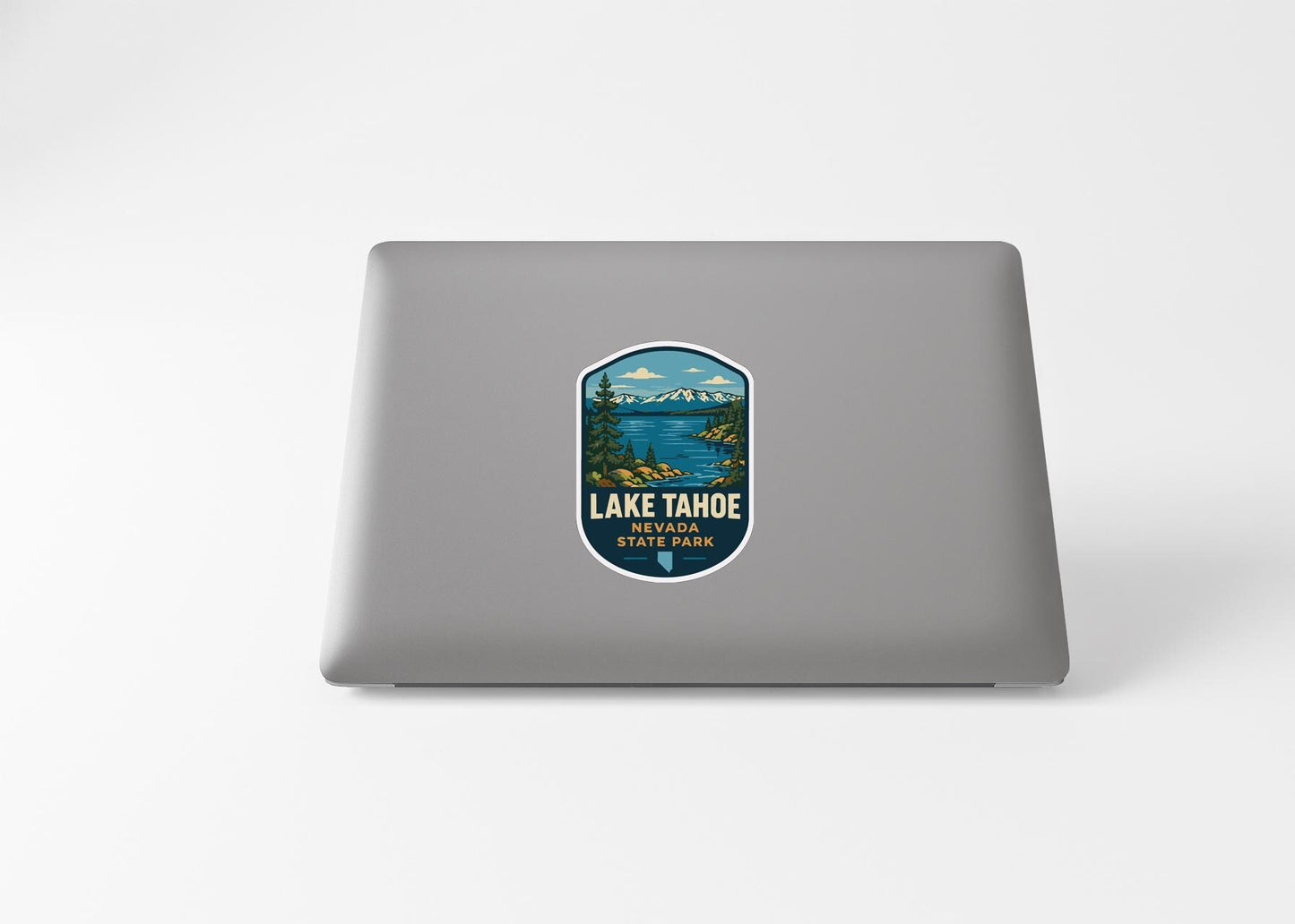 A sticker on the back of a laptop, depicting a scenic landscape with mountains, water, and a lake.