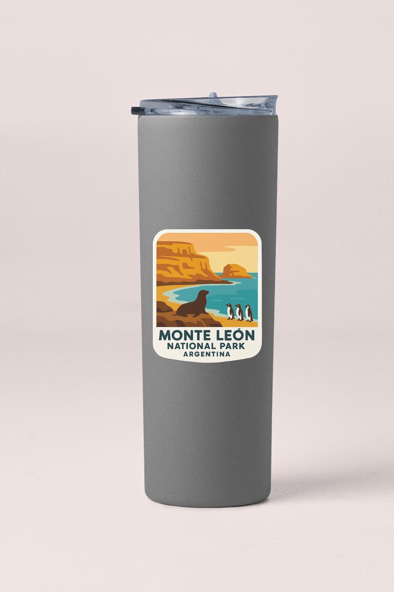 A gray insulated tumbler with a label that features an illustration of a scenic landscape with mountains, water, and penguins.
