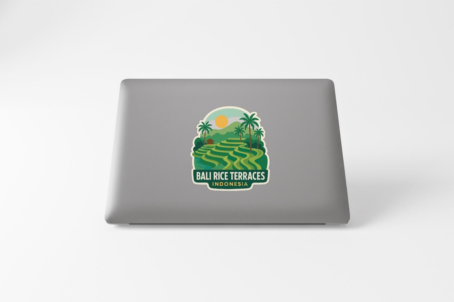 a sticker or decal on the back of a laptop, depicting a tropical landscape with palm trees, rice terraces, and a sun.