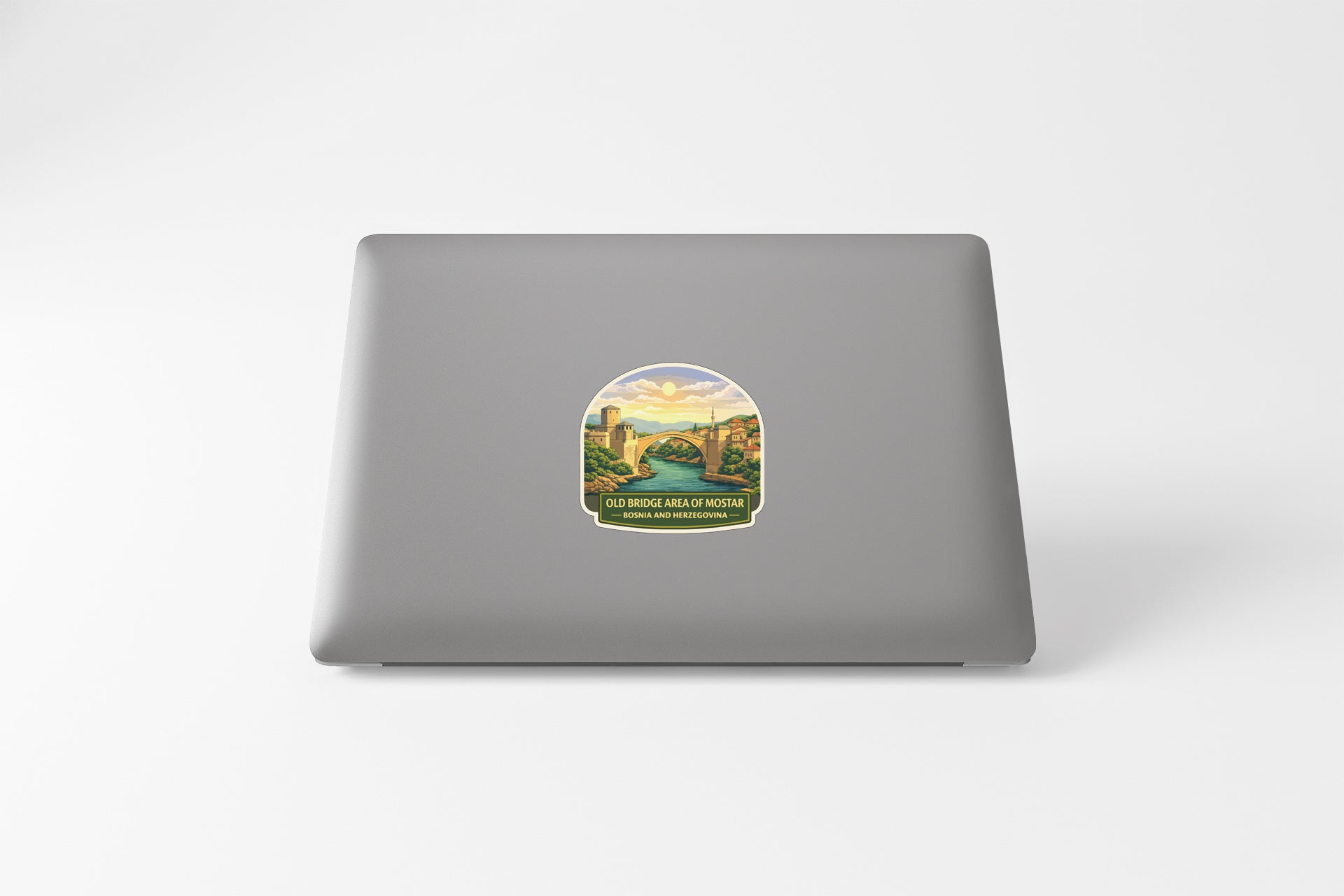 A sticker depicting a scenic landscape with a bridge and mountains is placed on the back of a laptop computer.