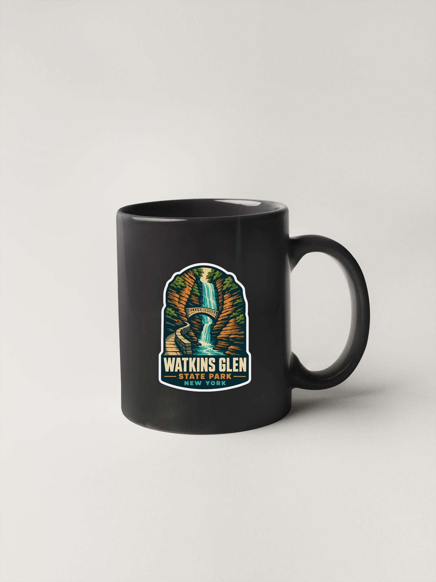 A black coffee mug with a colorful graphic and text logo that says "Watkins Glen State Park".
