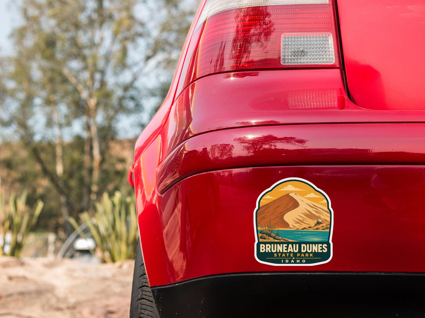 the rear end of a red car with a sticker on the back window that says "Bruneau Dunes State Park Idaho".