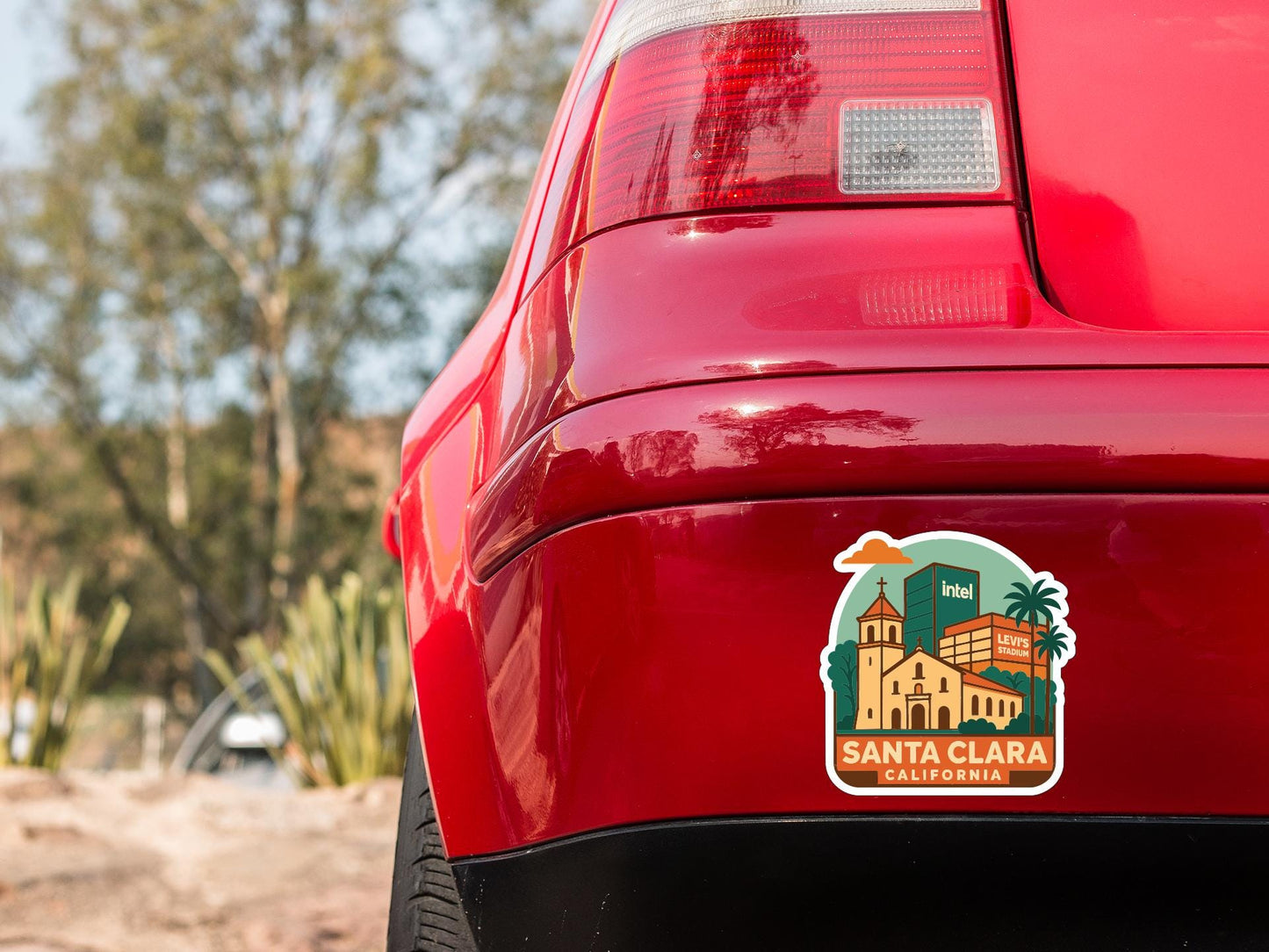 the rear end of a red car with a sticker on the trunk that features a cityscape and text.