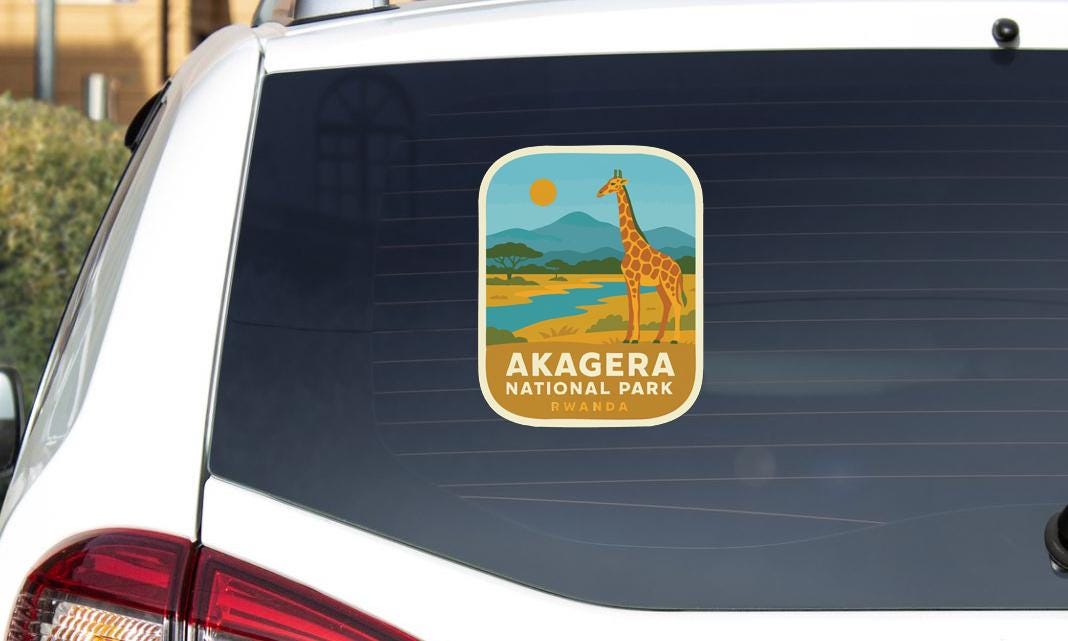 a sticker on the rear window of a vehicle, depicting a giraffe in a natural landscape with mountains in the background.