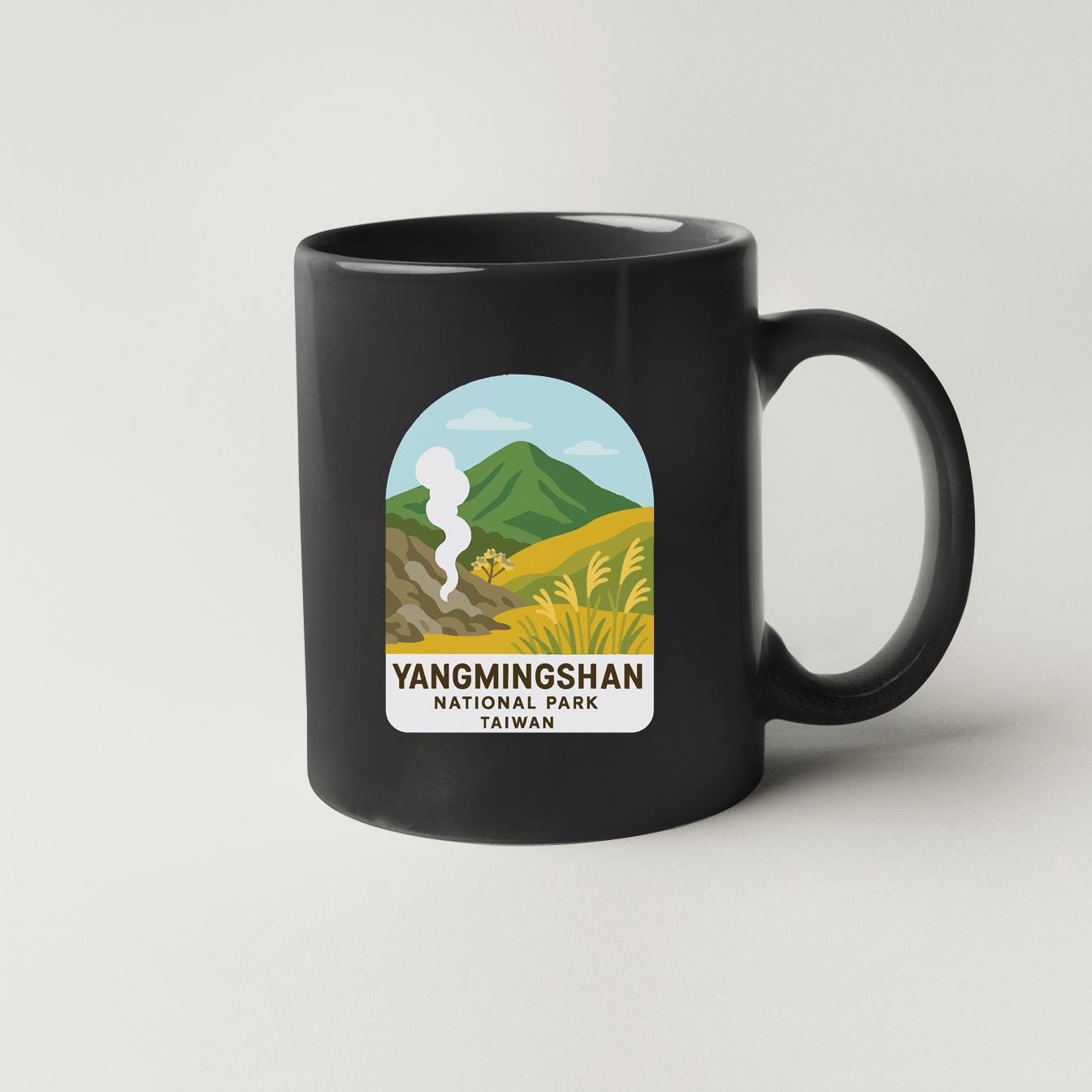 A black coffee mug with a graphic design depicting a scenic landscape with mountains, grass, and a steam rising from a mountain.