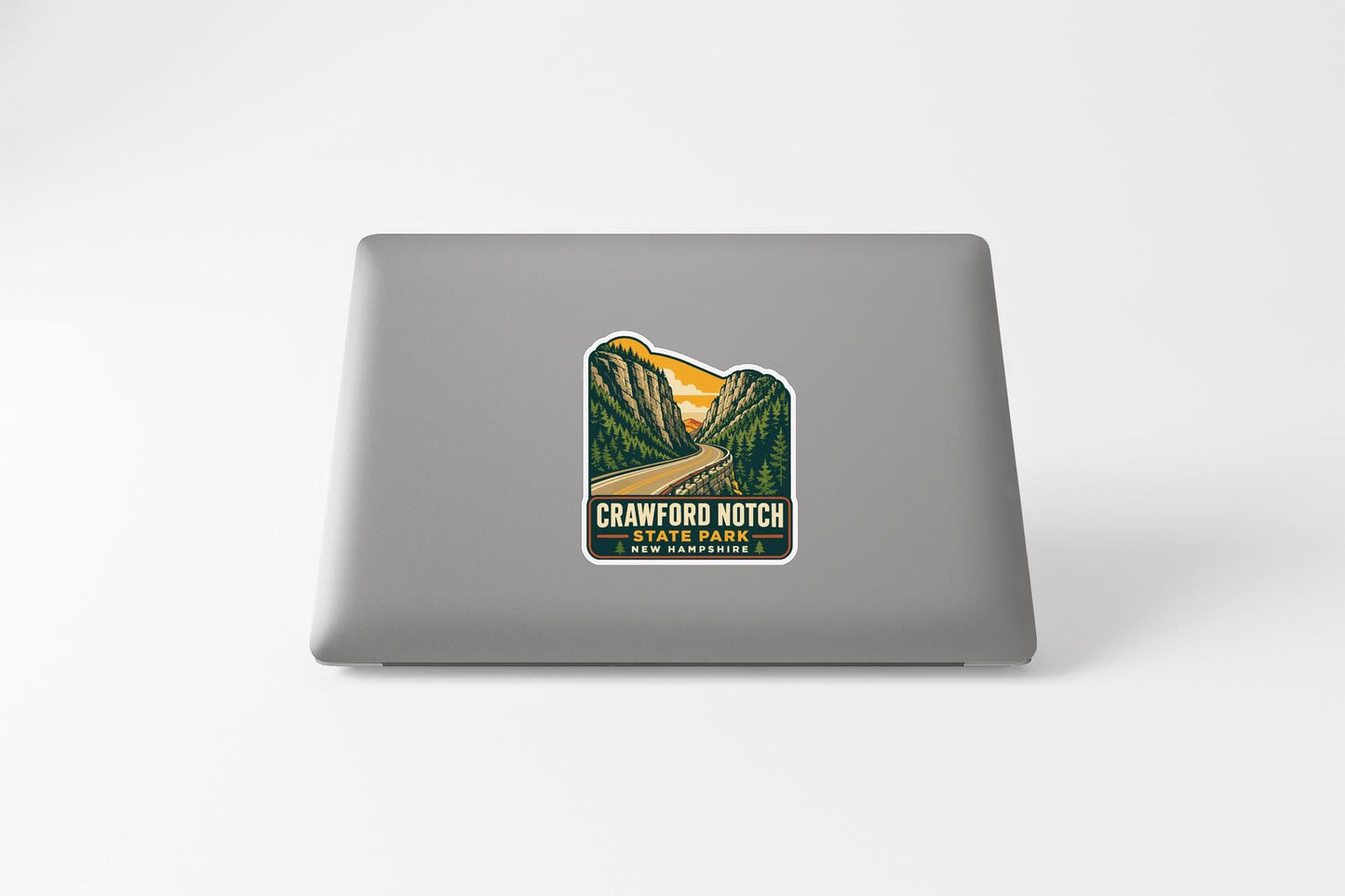 A sticker on the back of a laptop, depicting a scenic mountain landscape with a winding road leading through it.