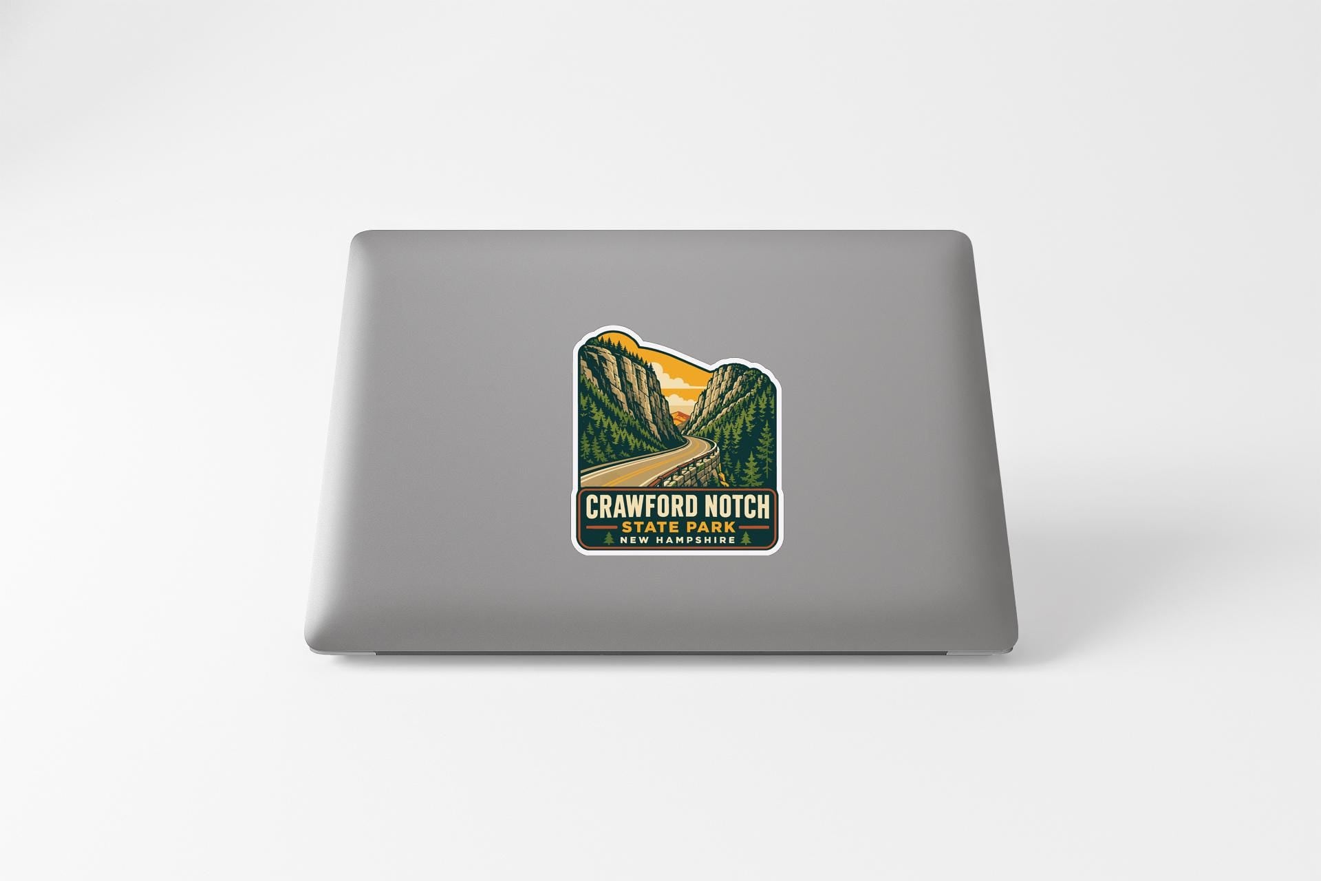 A sticker on the back of a laptop, depicting a scenic mountain landscape with a winding road leading through it.